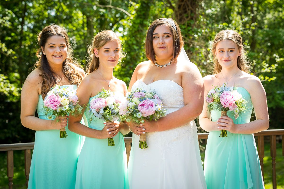 A wedding party in matching mint green bridesmaid dresses and white bridal gown pose outdoors holding flower bouquets.