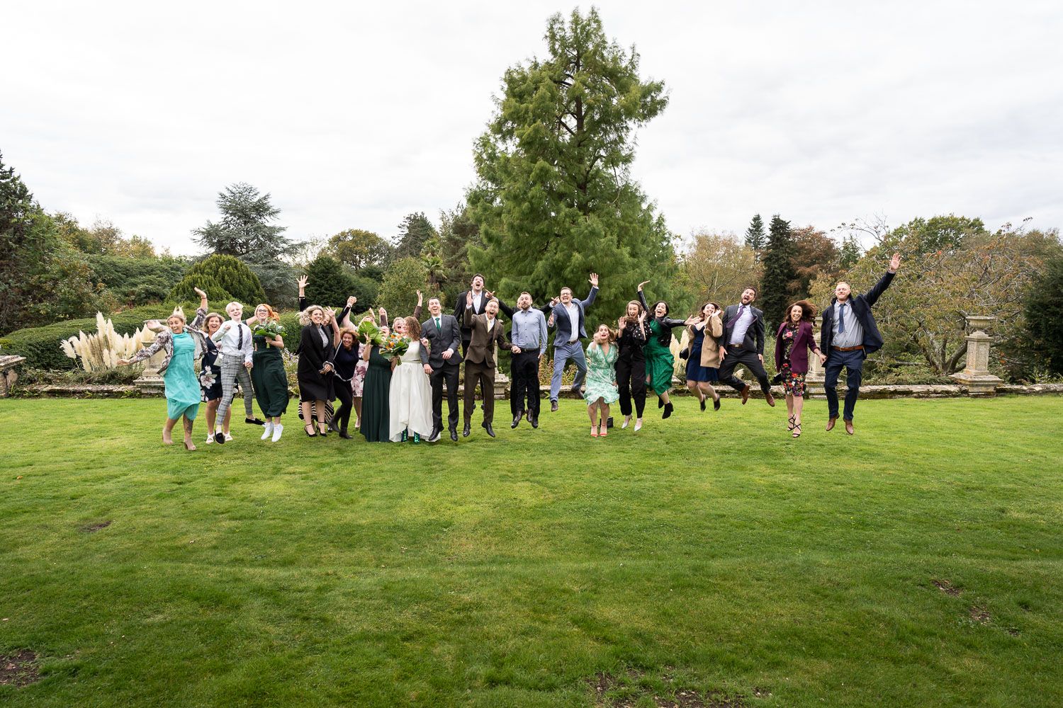 A large group of wedding guests gather on a lush green lawn for a formal outdoor photograph.