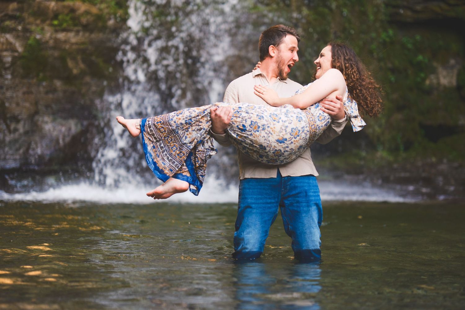 A couple shares a romantic moment in front of a waterfall as they stand in shallow water.