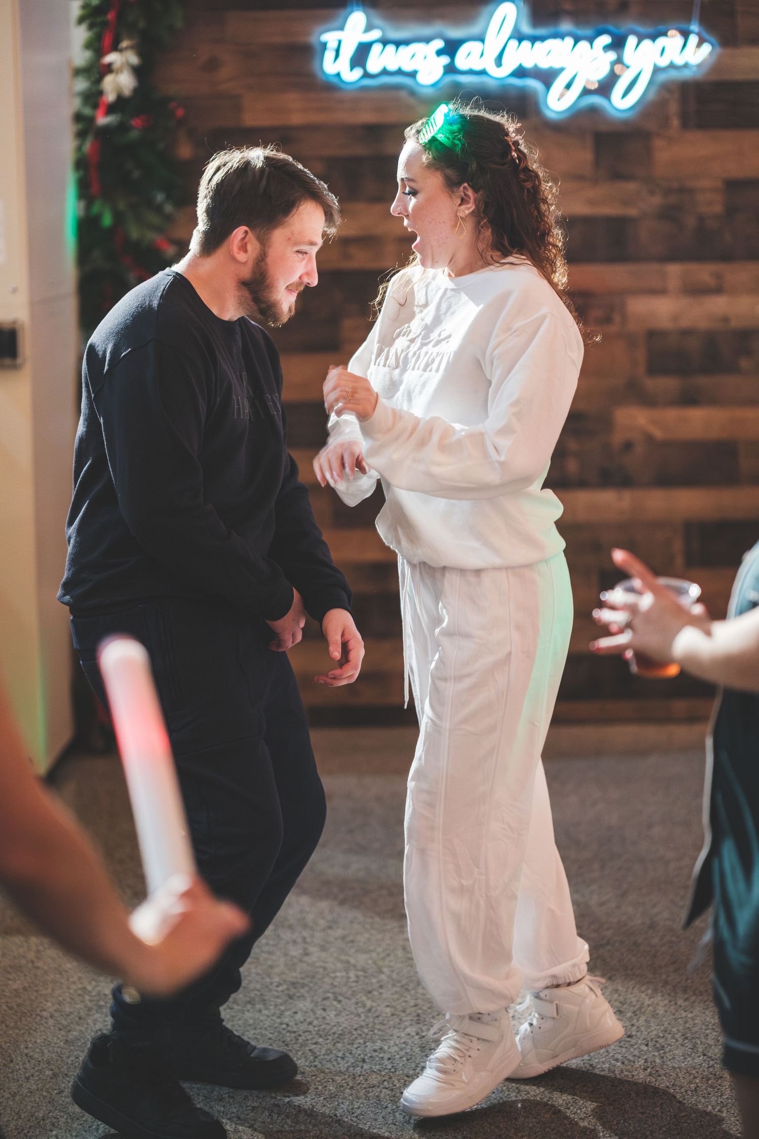 A smiling couple dances at a wedding reception under a glowing neon sign reading 