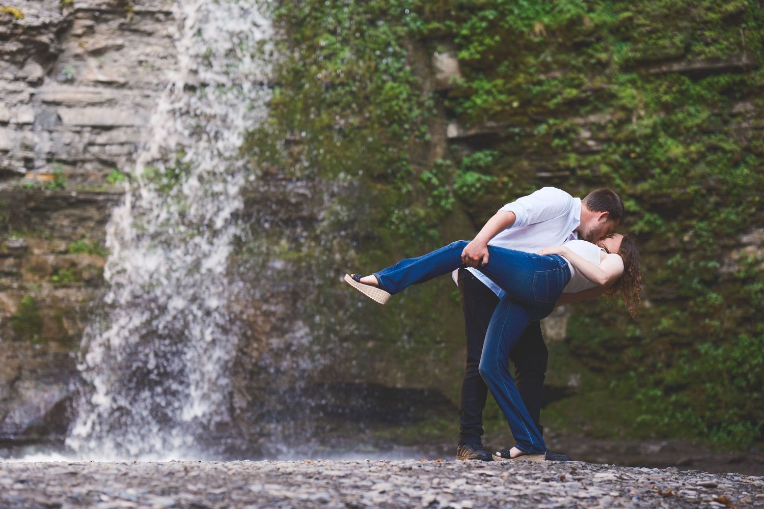 Man dips his partner in a romantic dance pose in front of a cascading waterfall for an adventurous engagement photo.