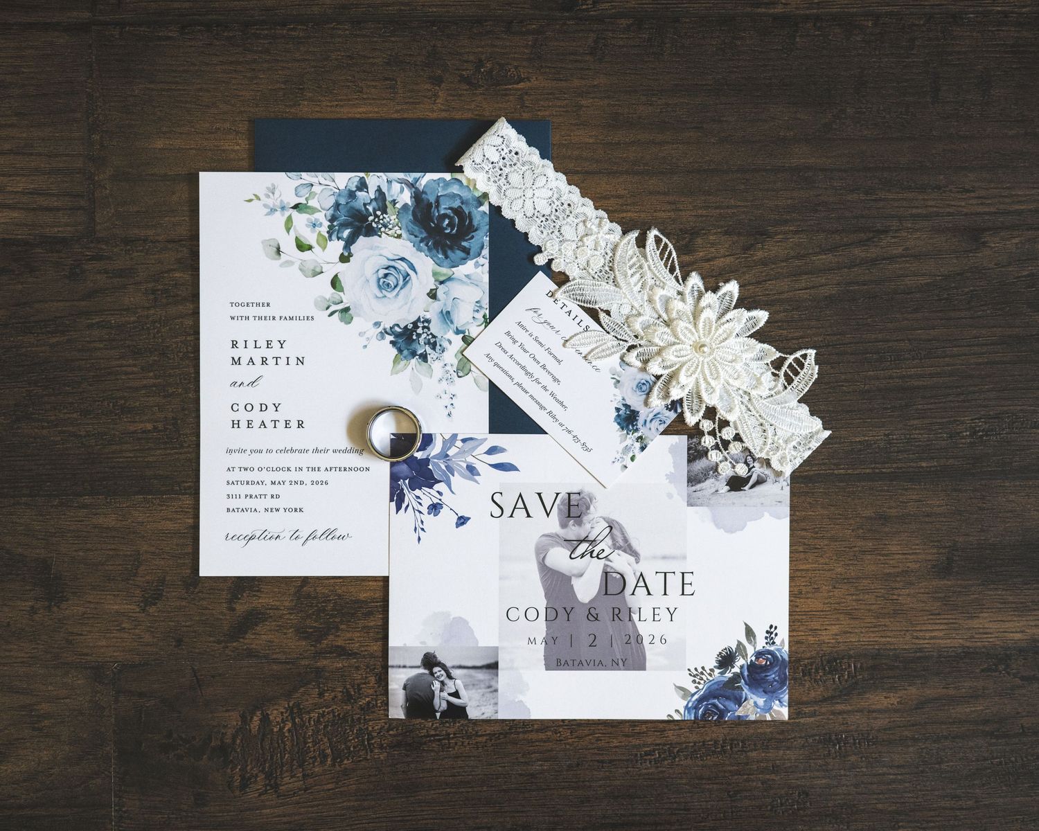 Navy and white floral wedding invitation suite with save the date card, ring, and lace floral garter arranged on a rustic dark wood table.