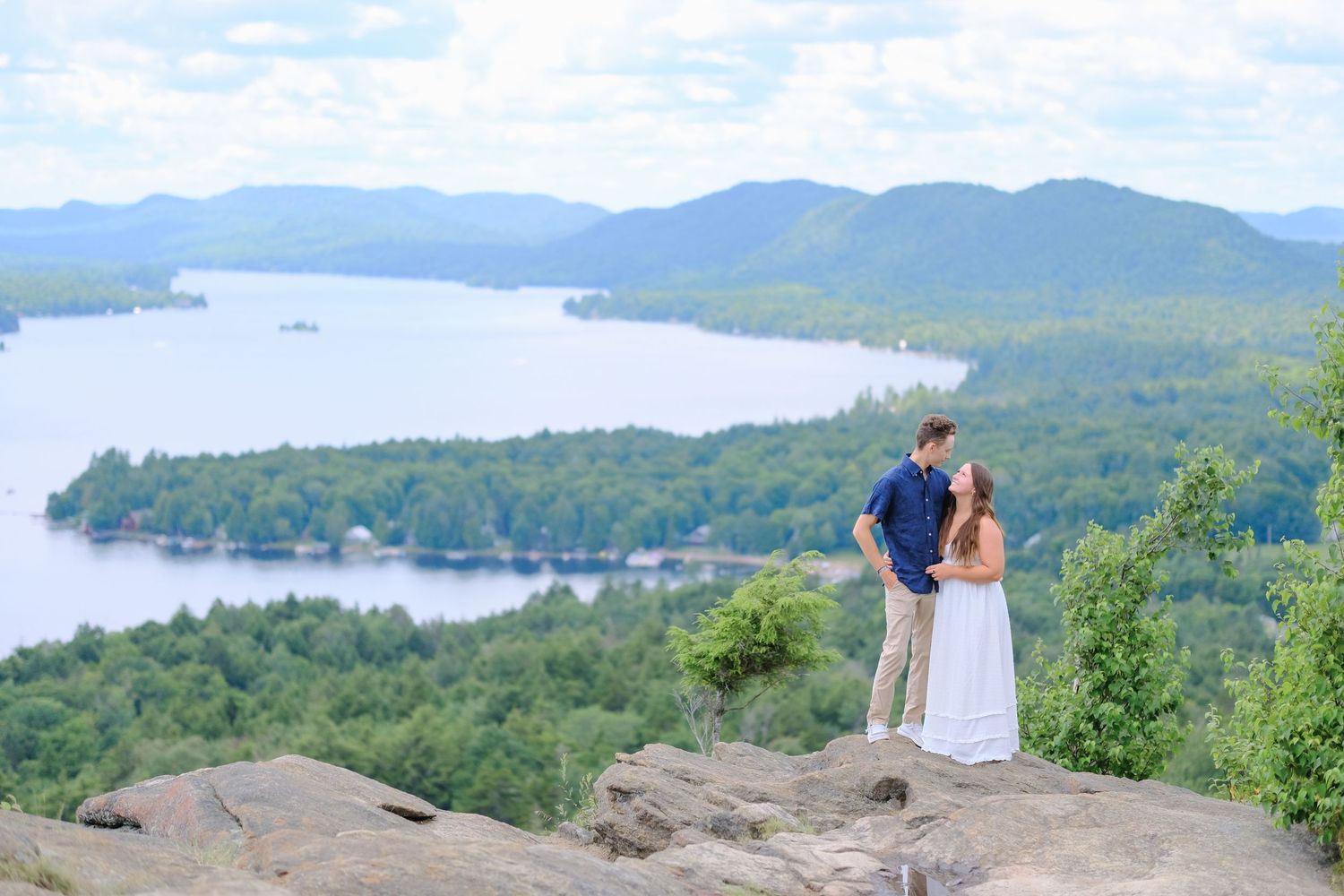 A couple stands on a mountain overlook admiring Fourth Lake and the Adirondack mountains in upstate New York.