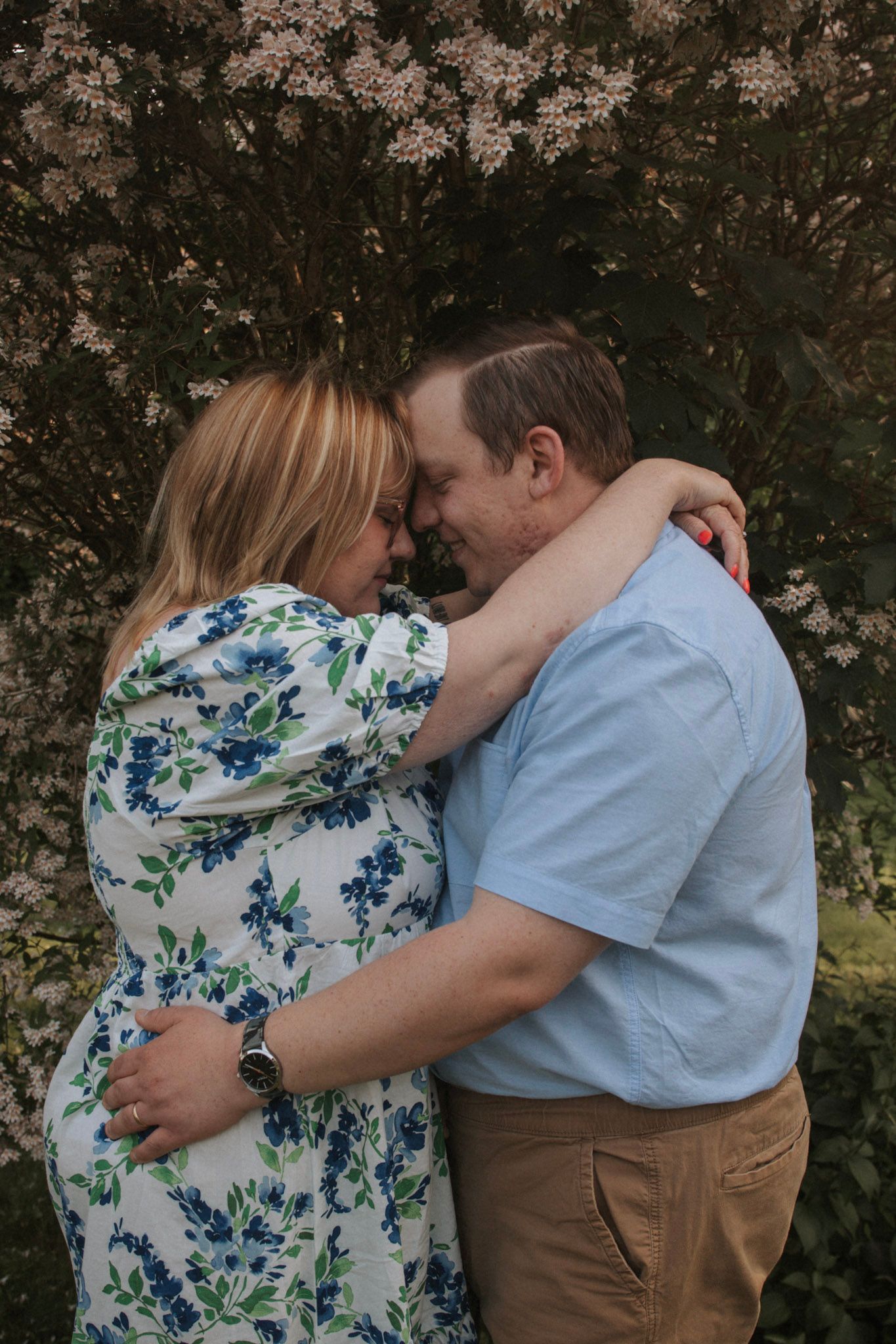 Romantic couple in a floral dress and casual attire share intimate moments against a blooming spring backdrop.