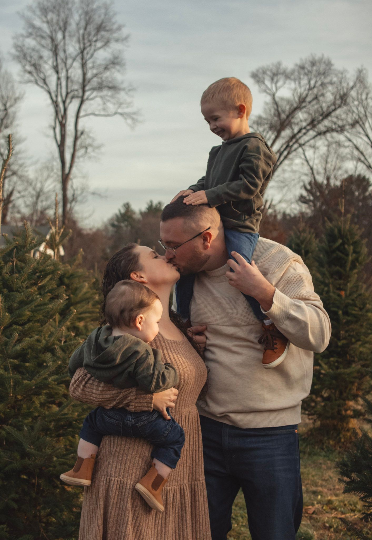 A family shares tender embraces and playful moments together at a Christmas tree farm on an overcast winter day.