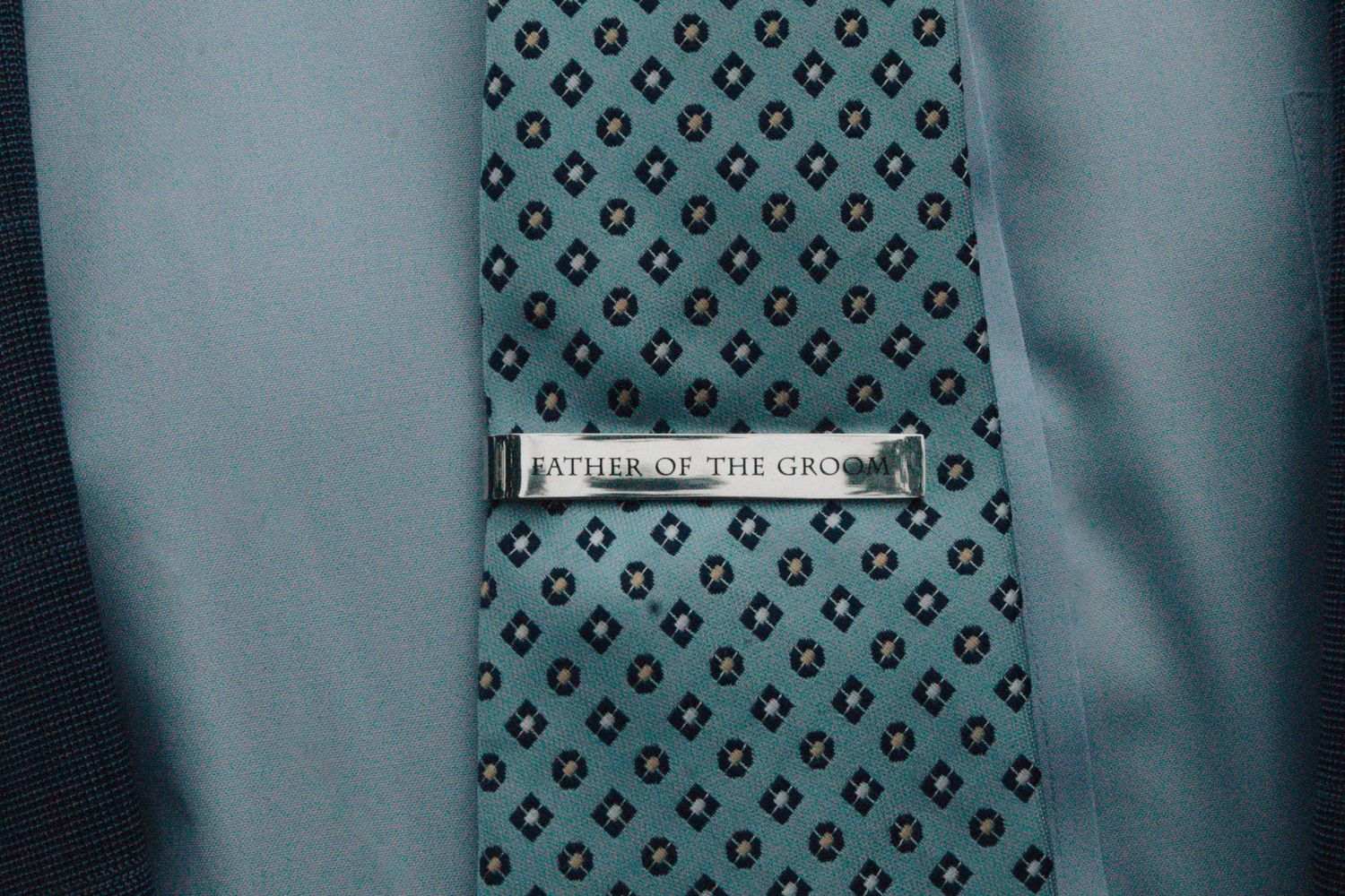 Close-up of a patterned tie with a silver tie clip reading 'I'll be there till the end'.