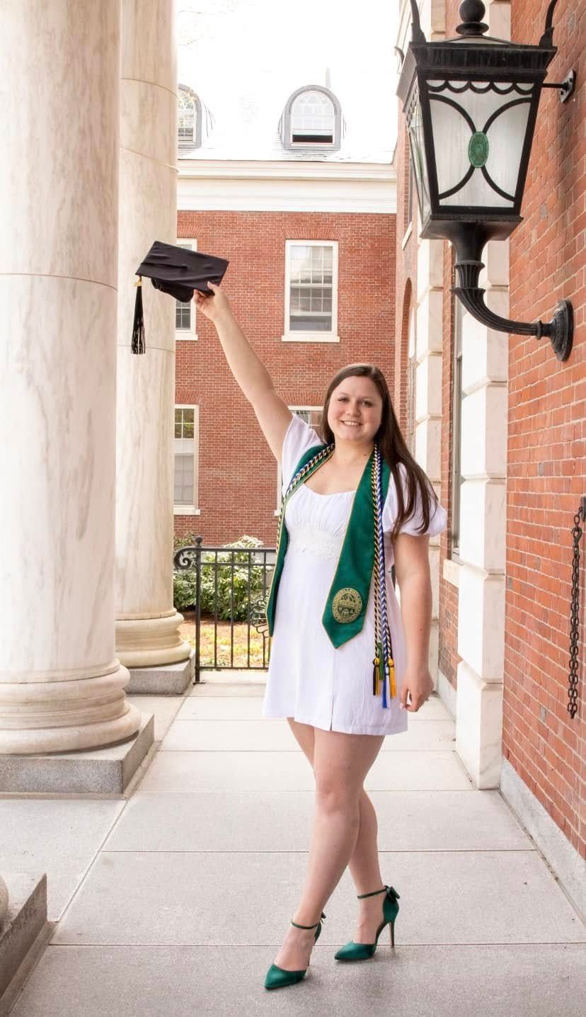 Graduate poses in white dress and green accessories between classic white columns.