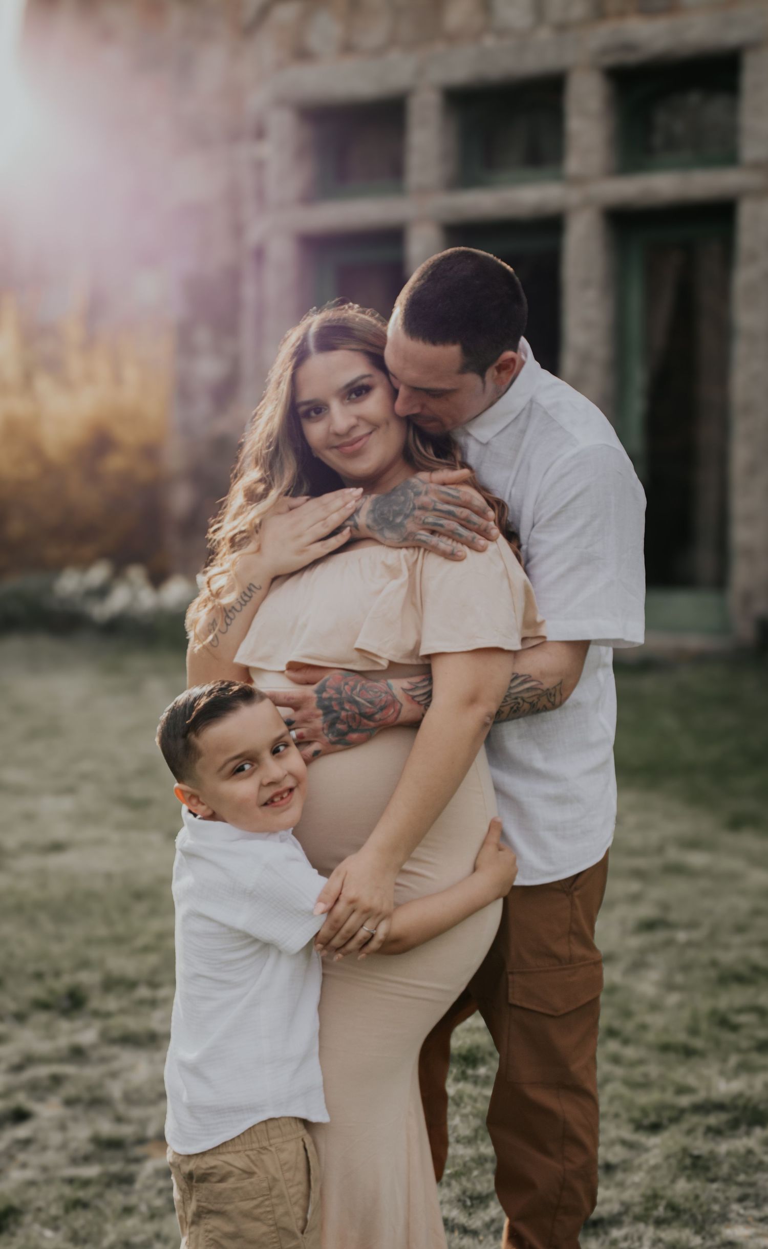 Family embracing during outdoor maternity photoshoot near rustic building.