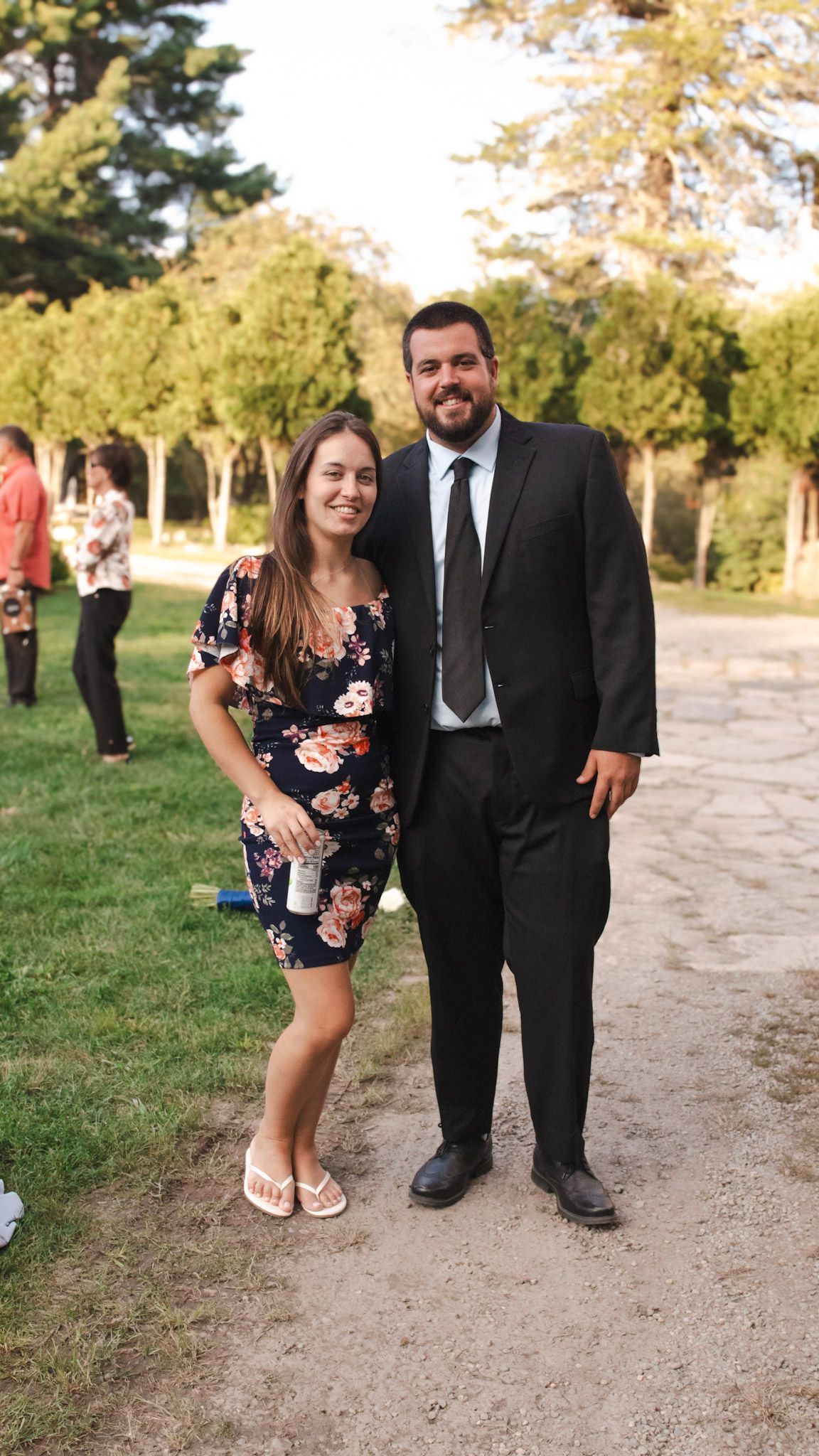 Couples pose together on a dirt path surrounded by lush green trees during golden hour.