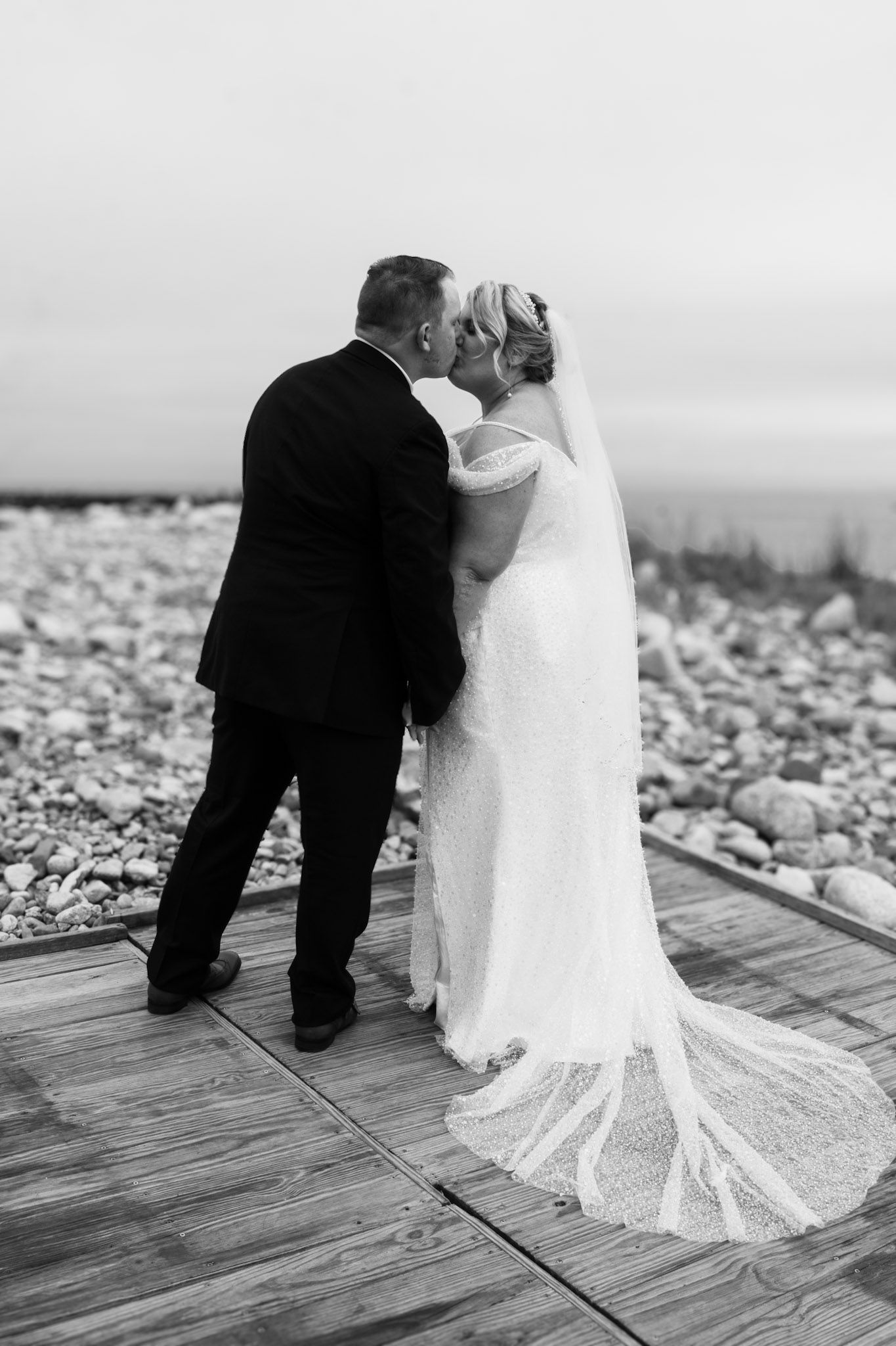 Black and white sequence of romantic wedding photos showing a couple on a wooden deck by a rocky beach.