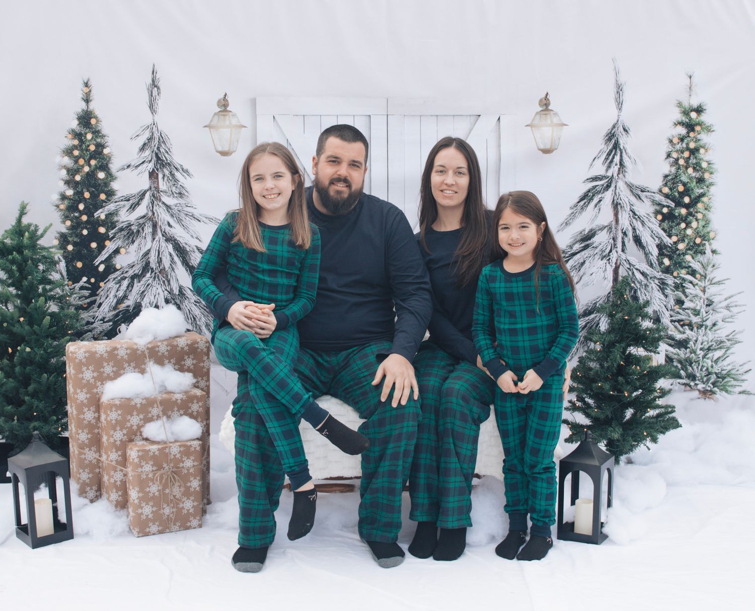 Family wearing matching green plaid outfits posing in snowy winter setting.