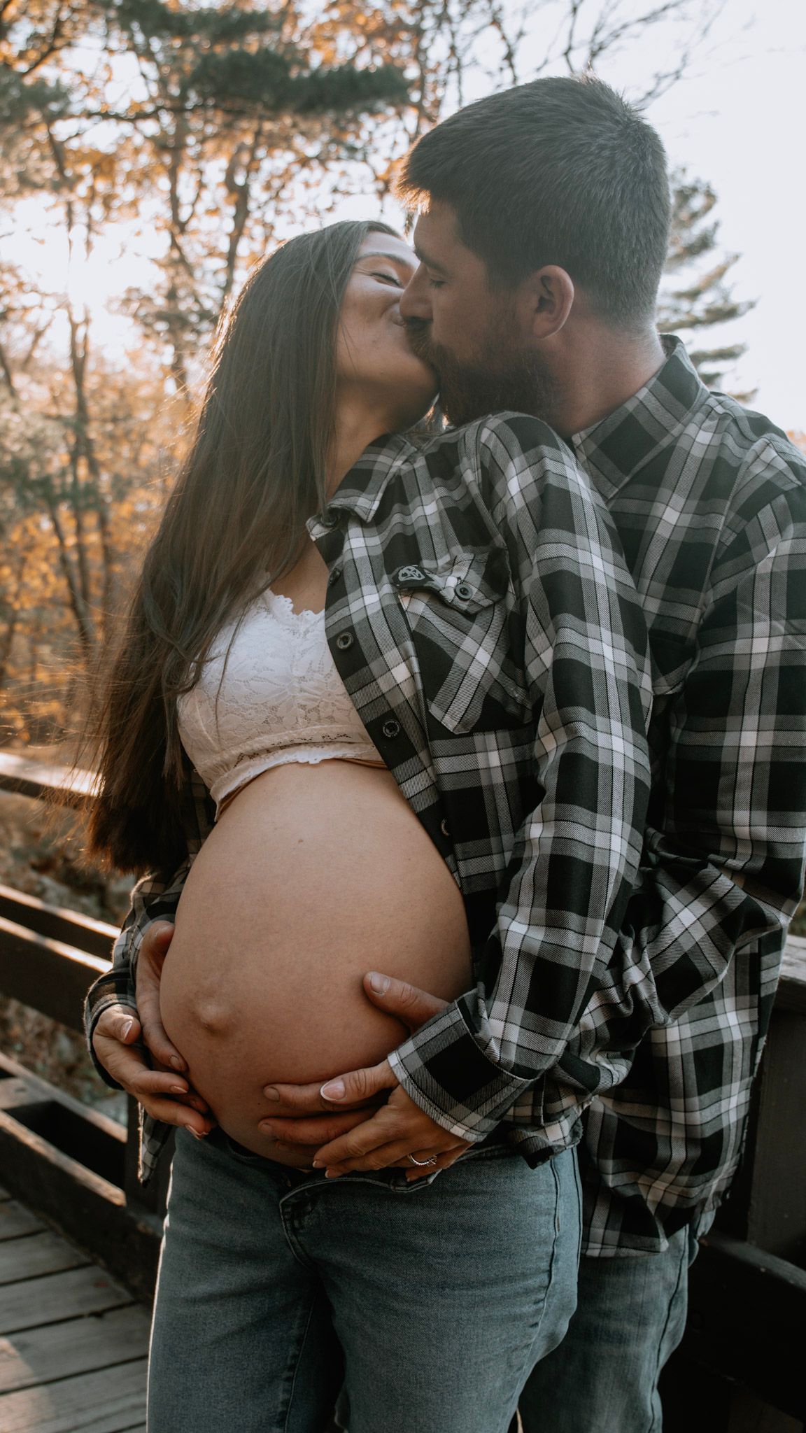 Intimate maternity photo series showing couple embracing on wooden deck during autumn sunset.