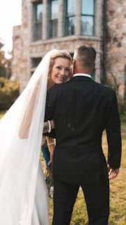 A bride in a flowing veil looks back over her shoulder while standing with her groom.