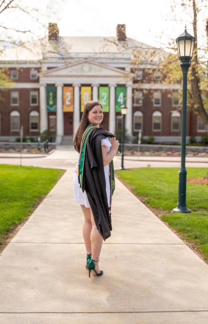 Graduate walking away on campus path with historic buildings in background.