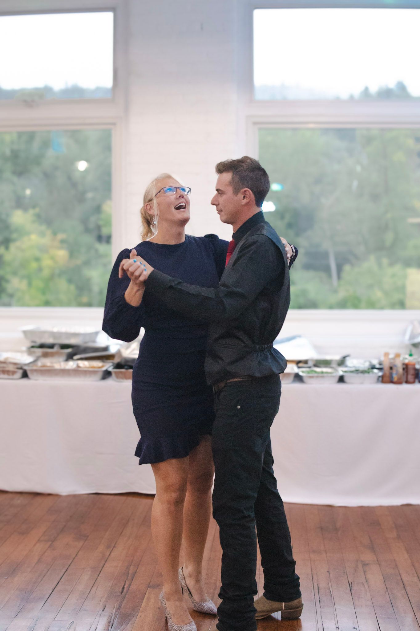 A couple dances together in a series of candid shots showing them laughing and embracing on a wooden dance floor.