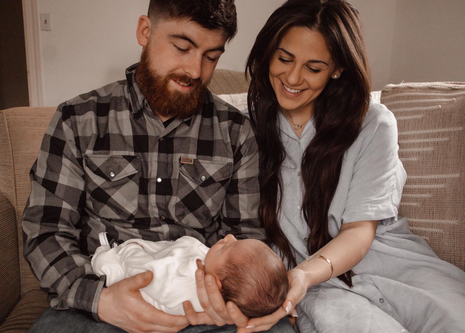 A family shares tender moments with their newborn on a couch.