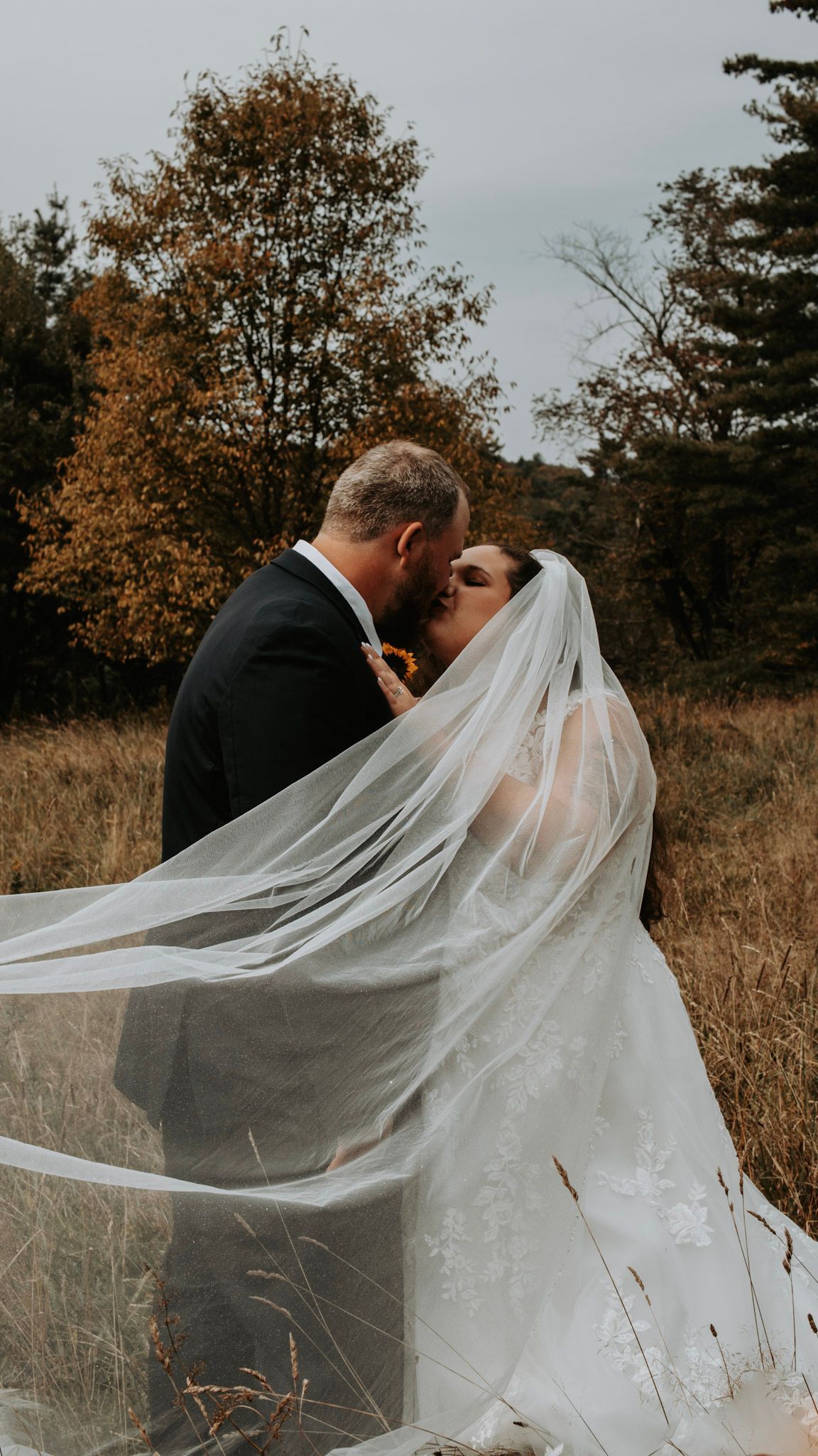 A romantic wedding moment captured with bride's veil flowing in the autumn breeze.