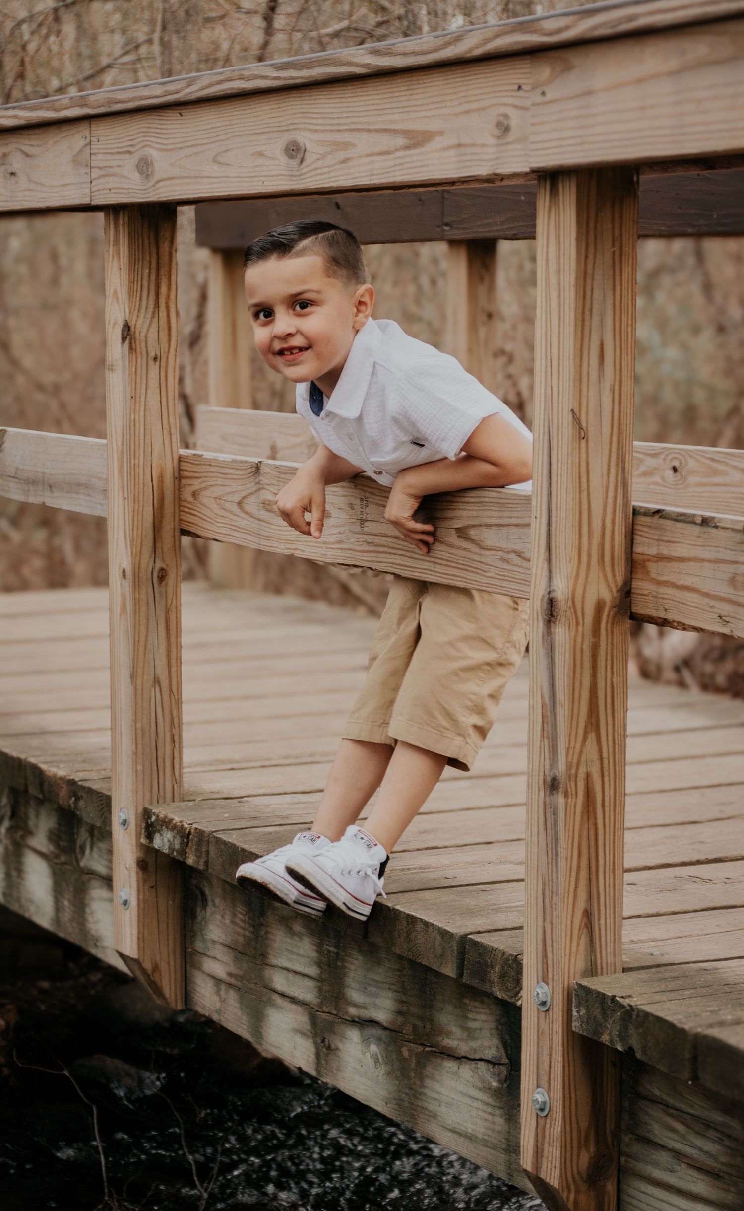 Young boy playfully poses on wooden bridge railing during outdoor photoshoot.
