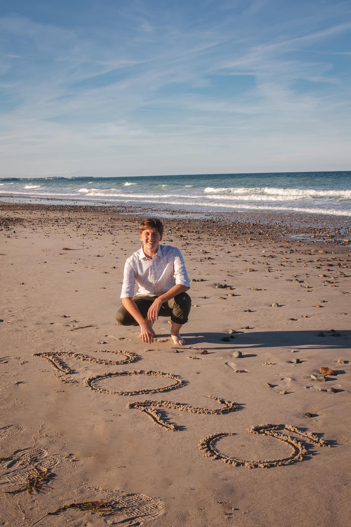 Beach engagement photos with heart shapes drawn in sand near ocean waves.