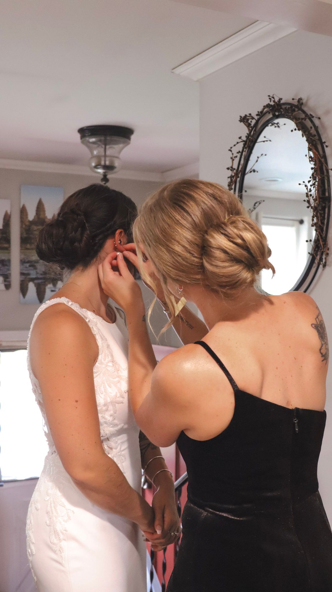 Bridesmaids in black dresses help adjust a wedding gown in a brightly lit dressing room.