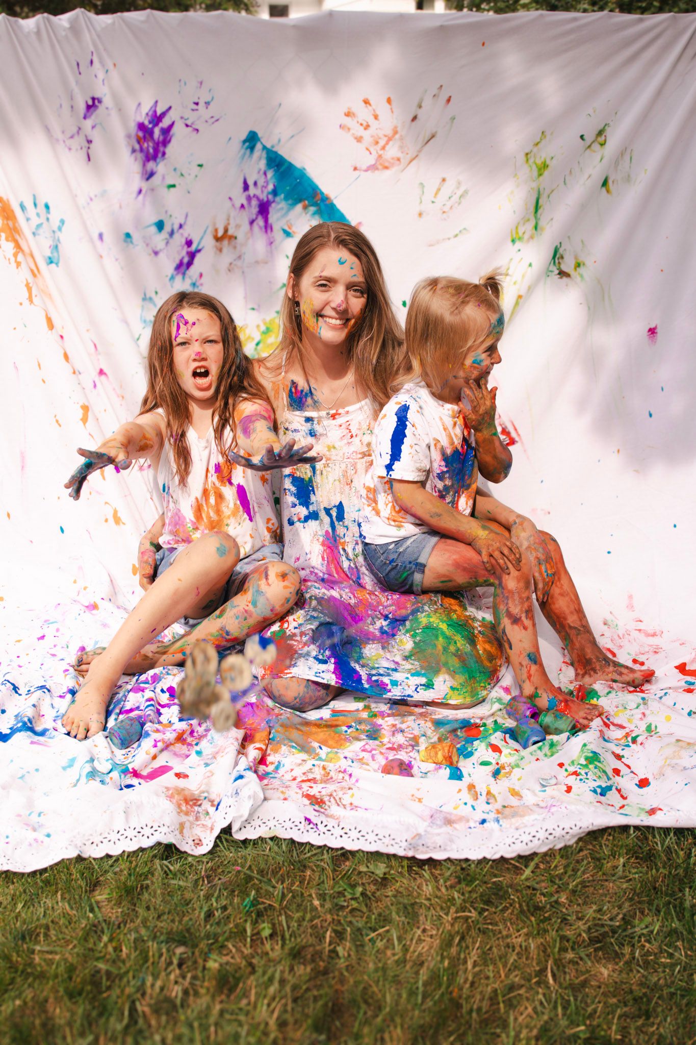 Joyful paint splatter photo shoot with colorful handprints and paint splatters against white backdrop on grass.