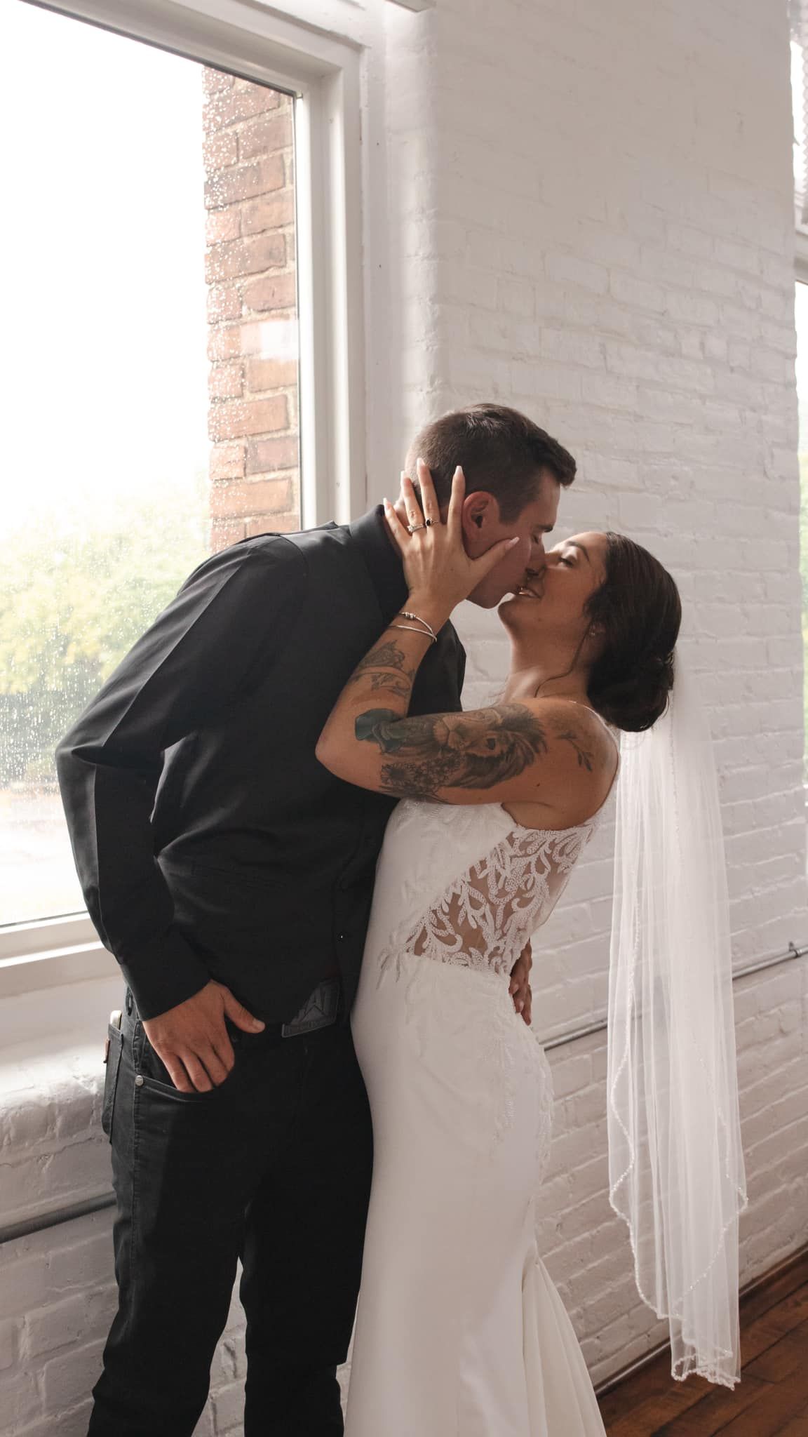 Romantic wedding moment captured near a window with exposed brick and natural lighting.