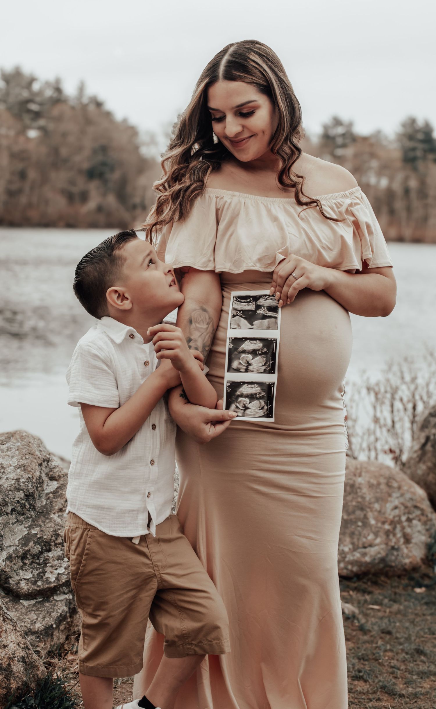 Pregnancy announcement photoshoot showing ultrasound photo by a lake in warm earth tones.