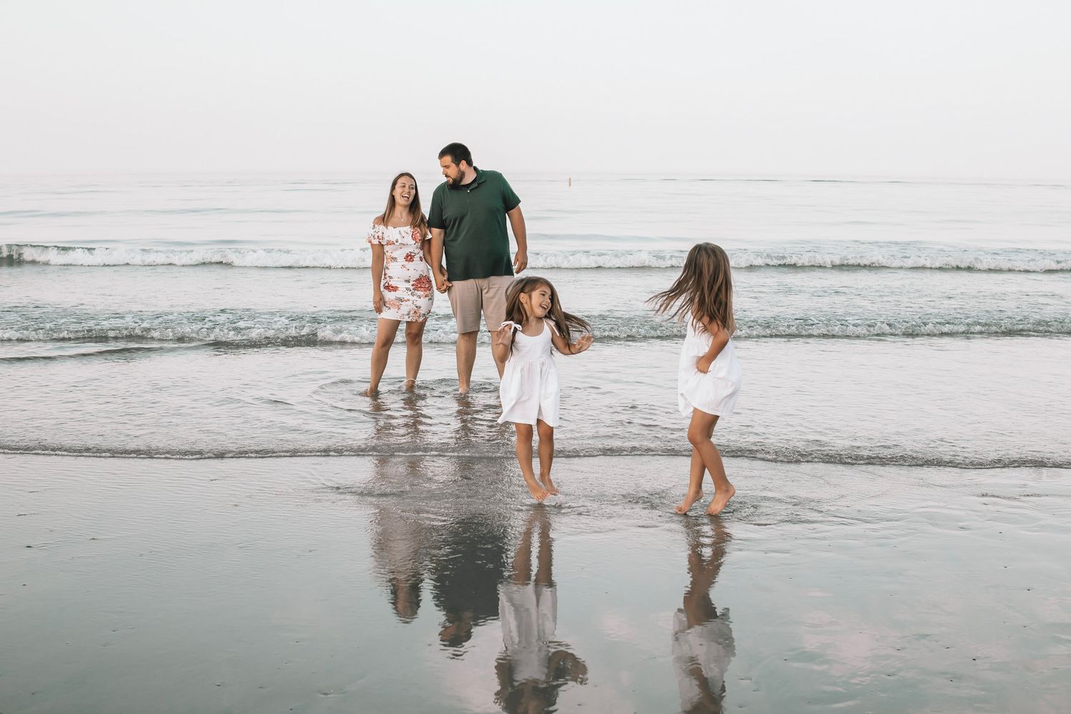 Family walking together on a misty beach shoreline with waves and reflections in the wet sand.