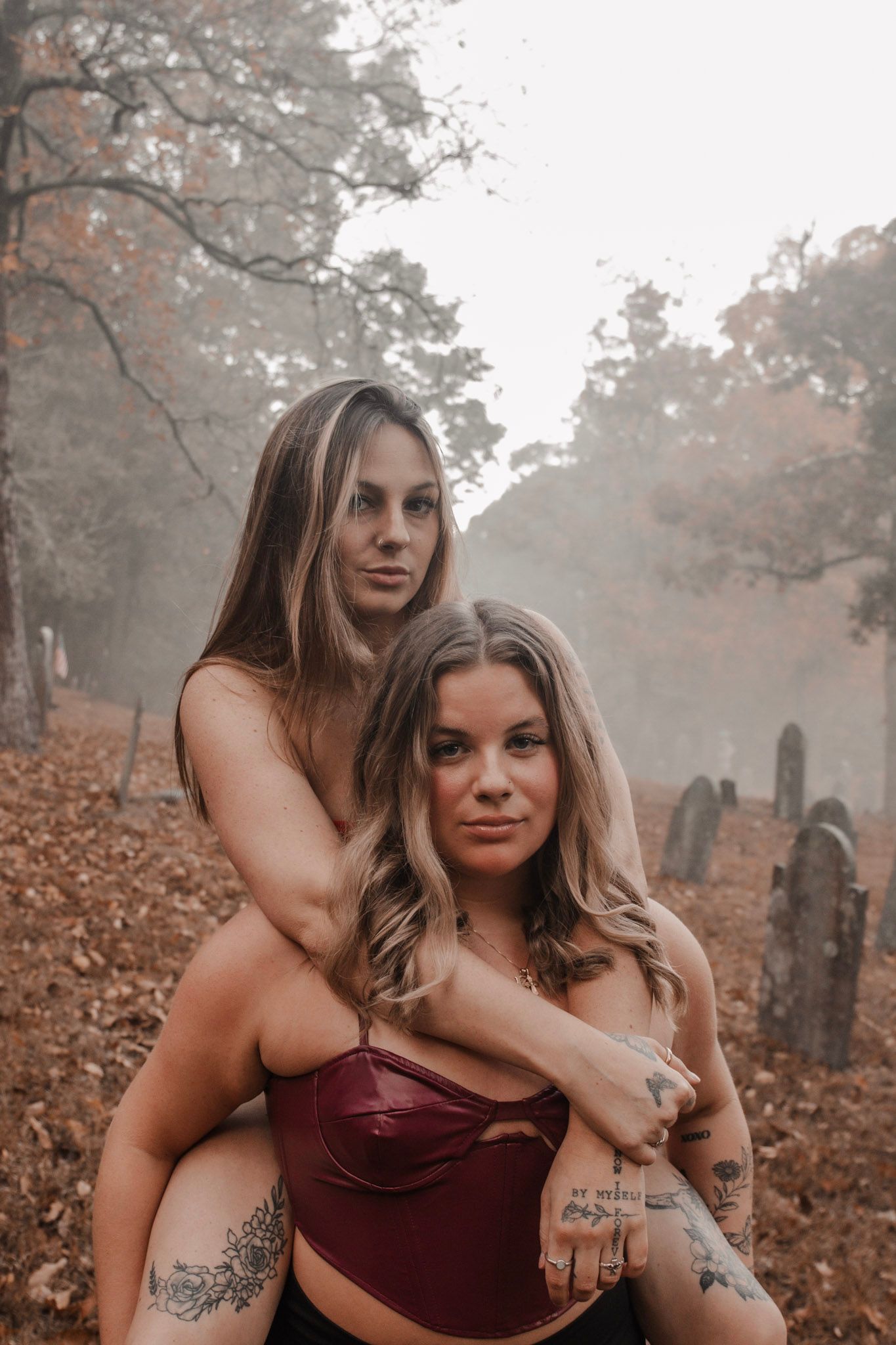 Two people share an intimate moment among autumn leaves and fog in a moody forest setting.