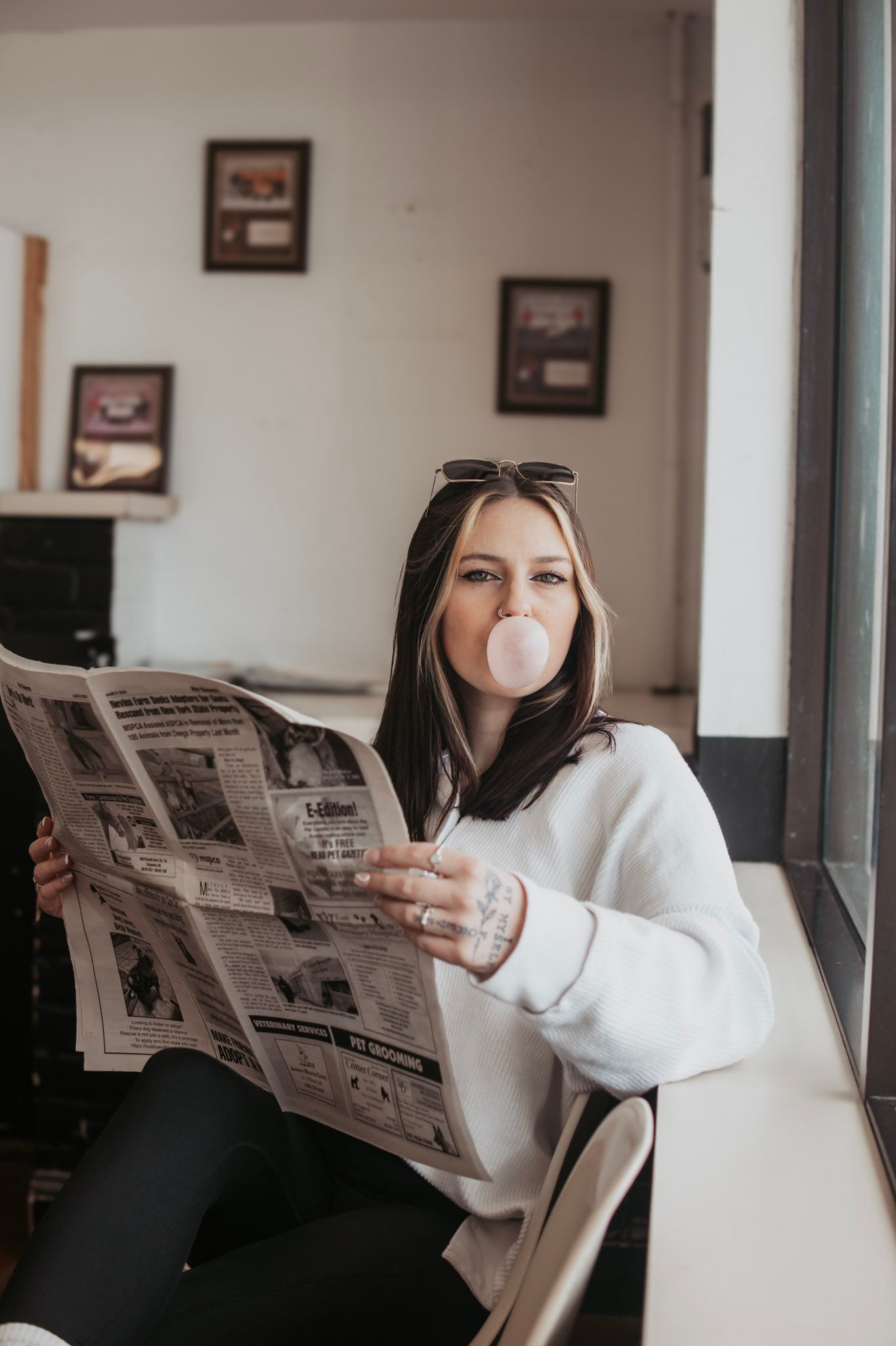 Person in white sweater reading newspaper while relaxing at home in natural lighting.