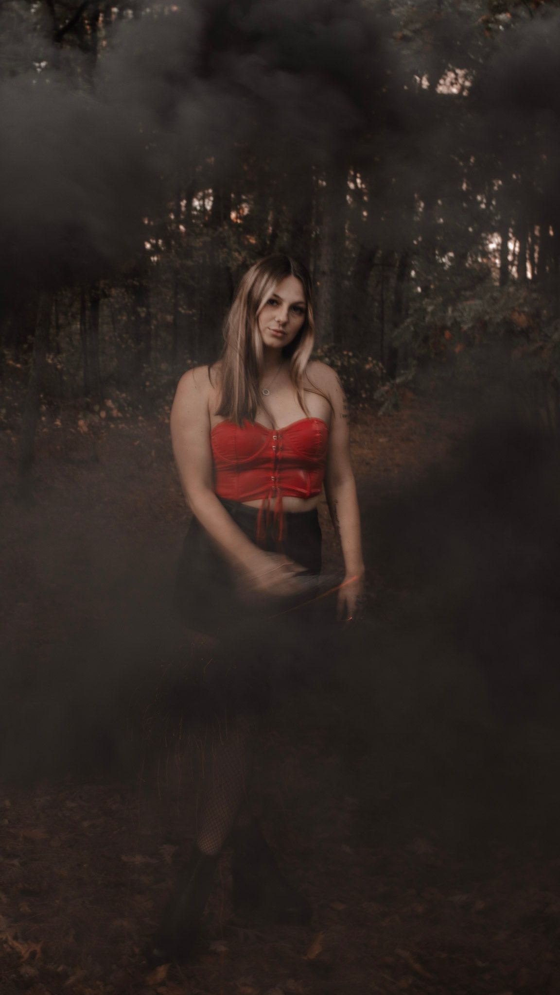 Moody forest photoshoot featuring a person in a red corset top among dark autumn trees.
