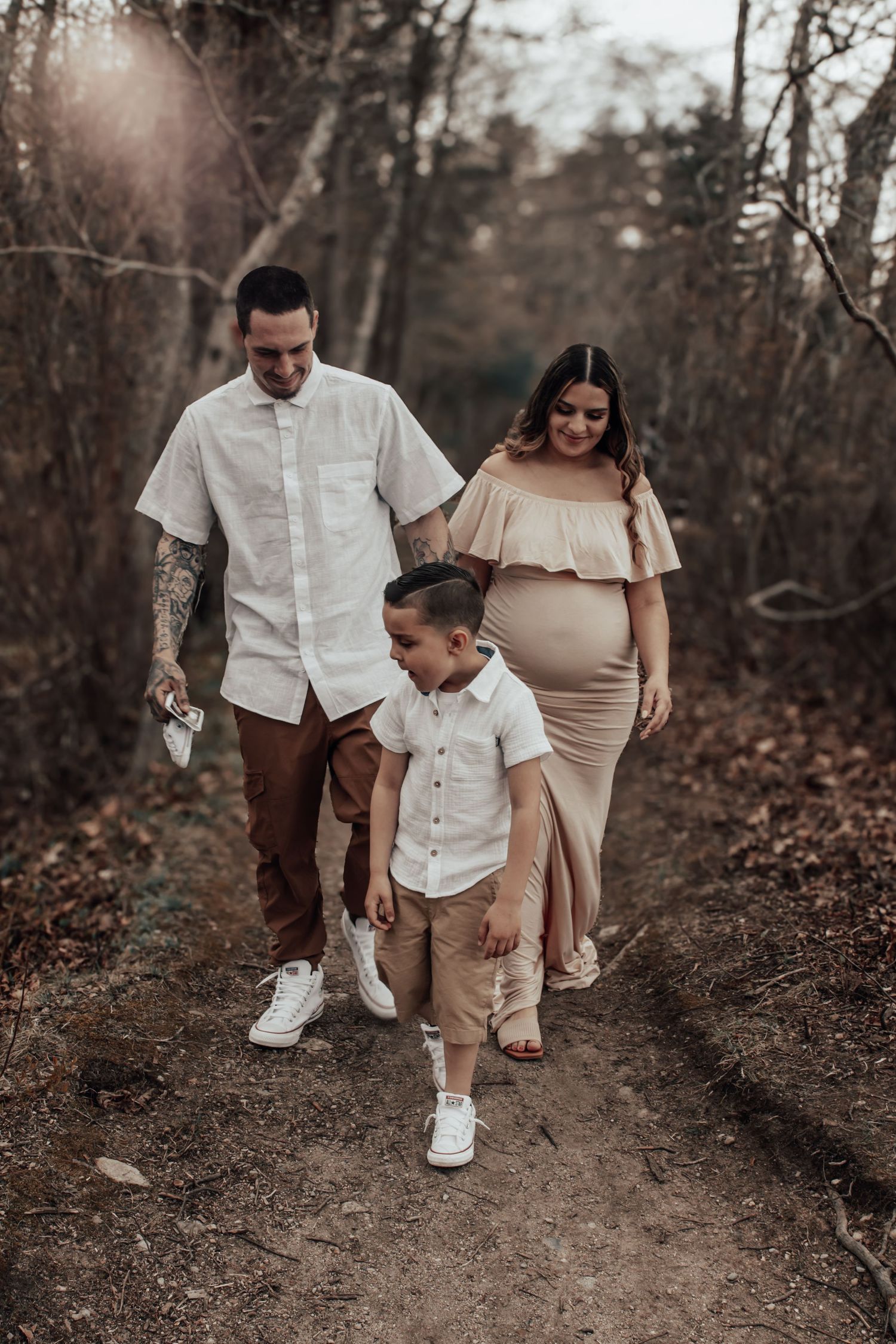 Family walks together on forest trail during autumn maternity photoshoot.