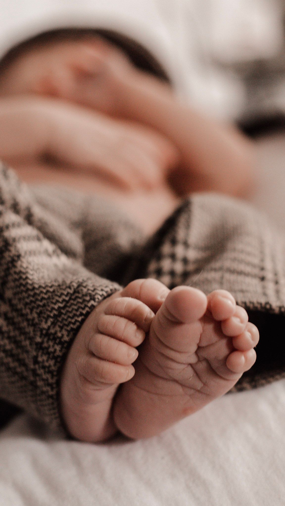 Close-up view of tiny baby feet wrapped in a plaid blanket while resting on white bedding.