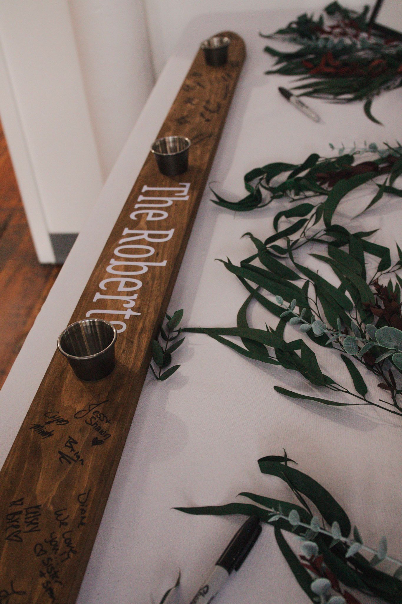 Rustic wooden beam decorated with scattered green foliage and handwritten messages.