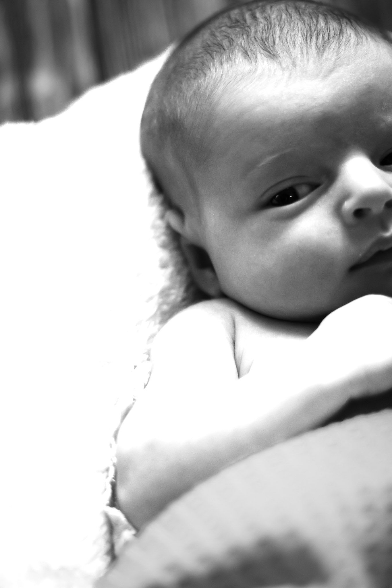 A black and white close-up portrait of a baby's face partially visible against a light background.