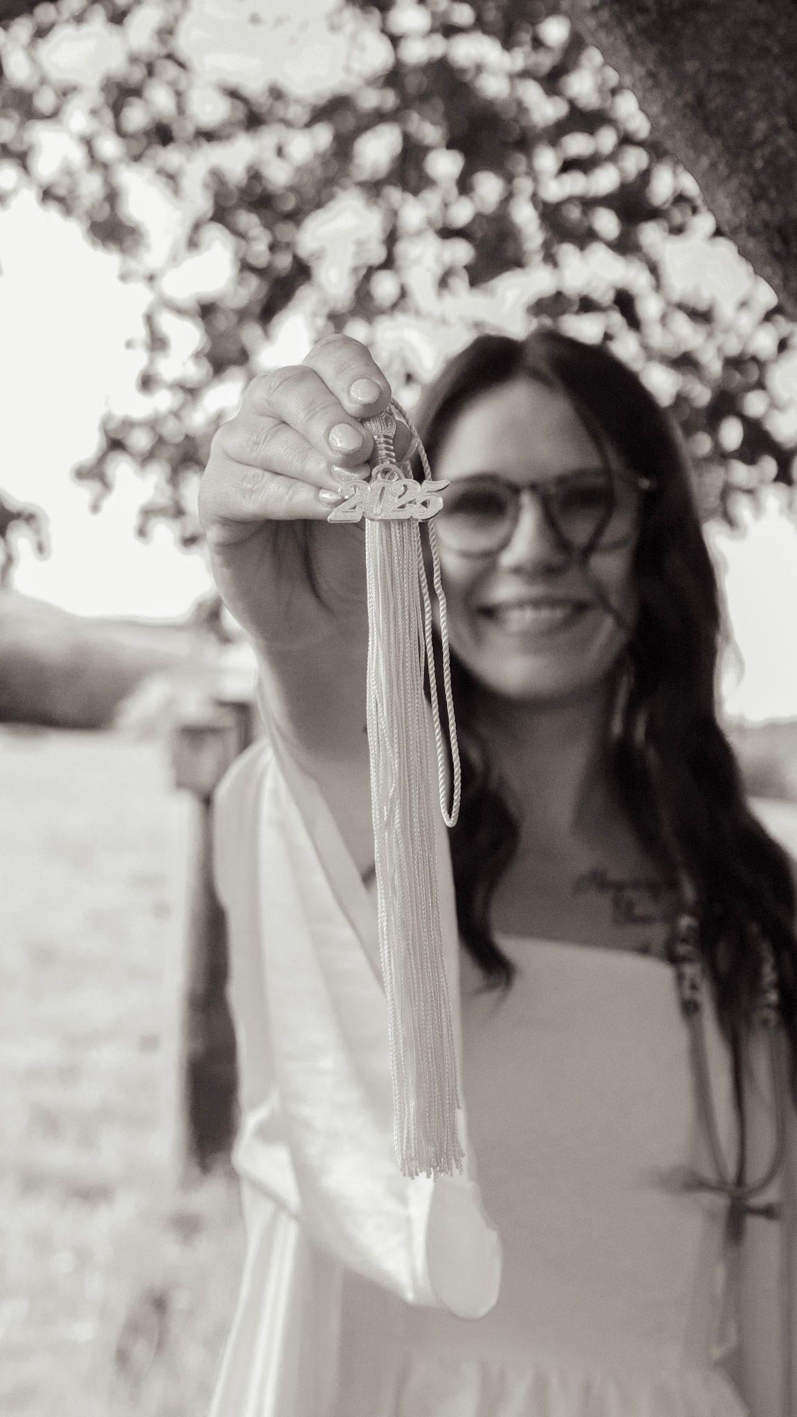 Black and white photo series showing someone in a light-colored dress holding graduation tassels outdoors.