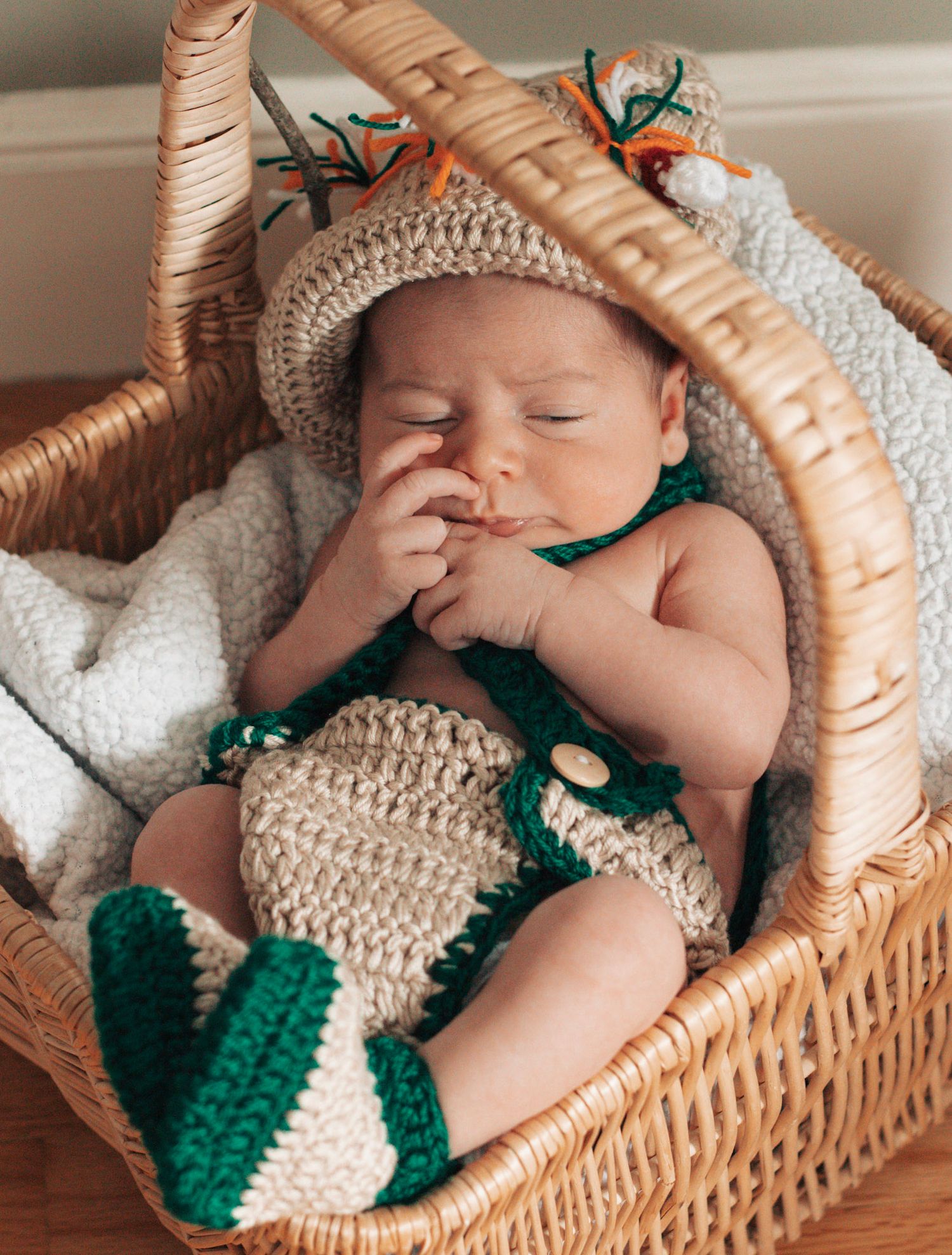 Peaceful newborn sleeping in wicker basket wearing crocheted green and white outfit.