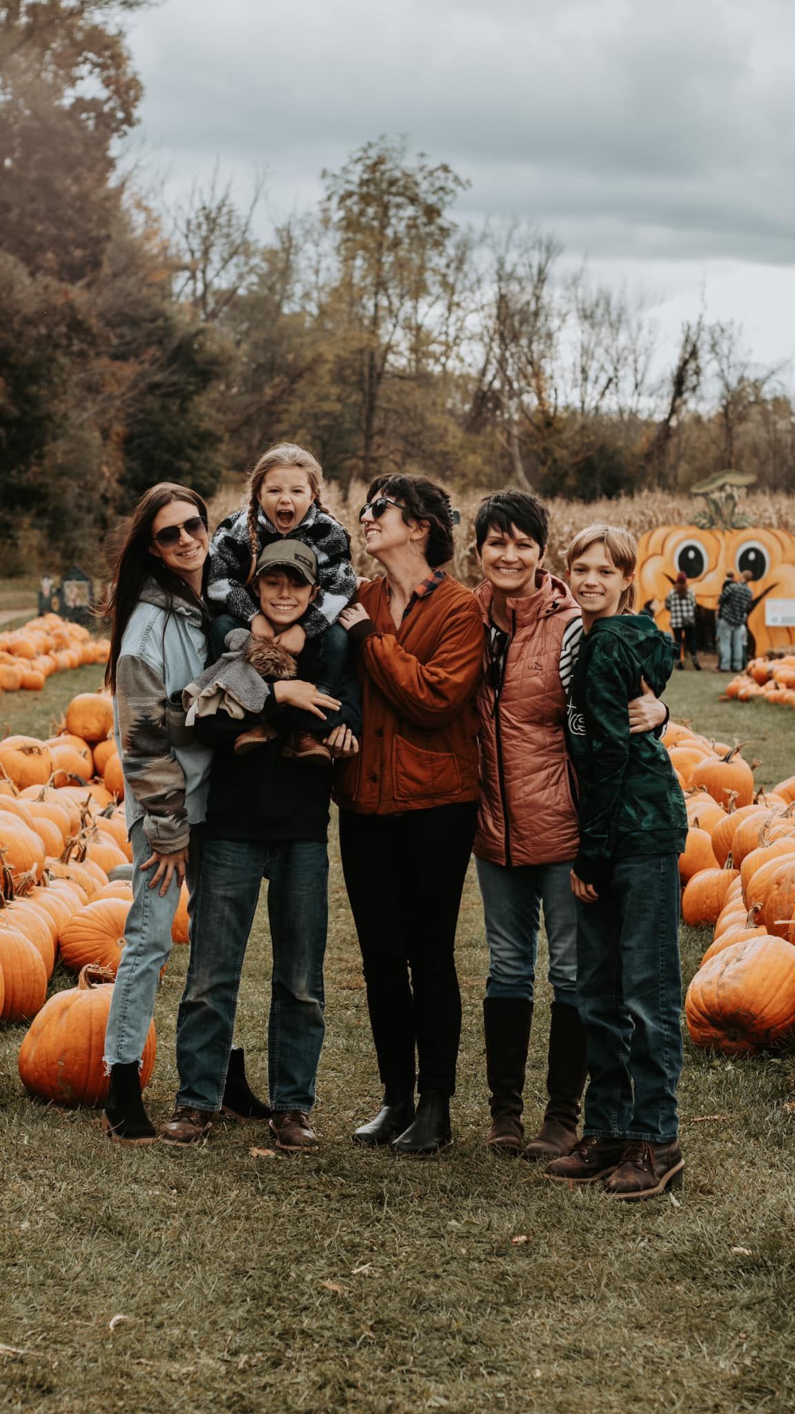 Group gathered for fun fall photo at pumpkin patch with cloudy sky.