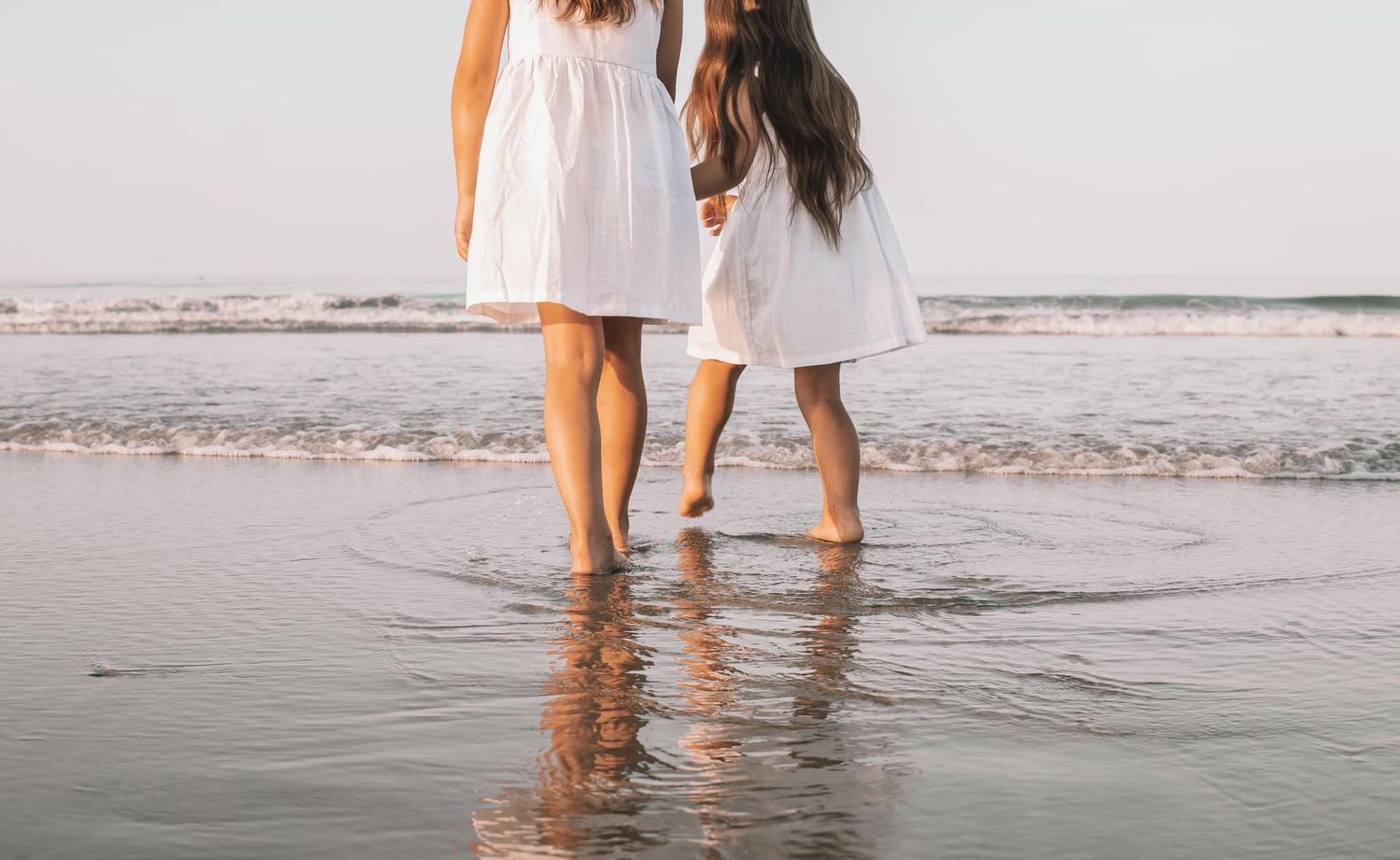 Couple walking along the beach shoreline at sunset with feet in the water.
