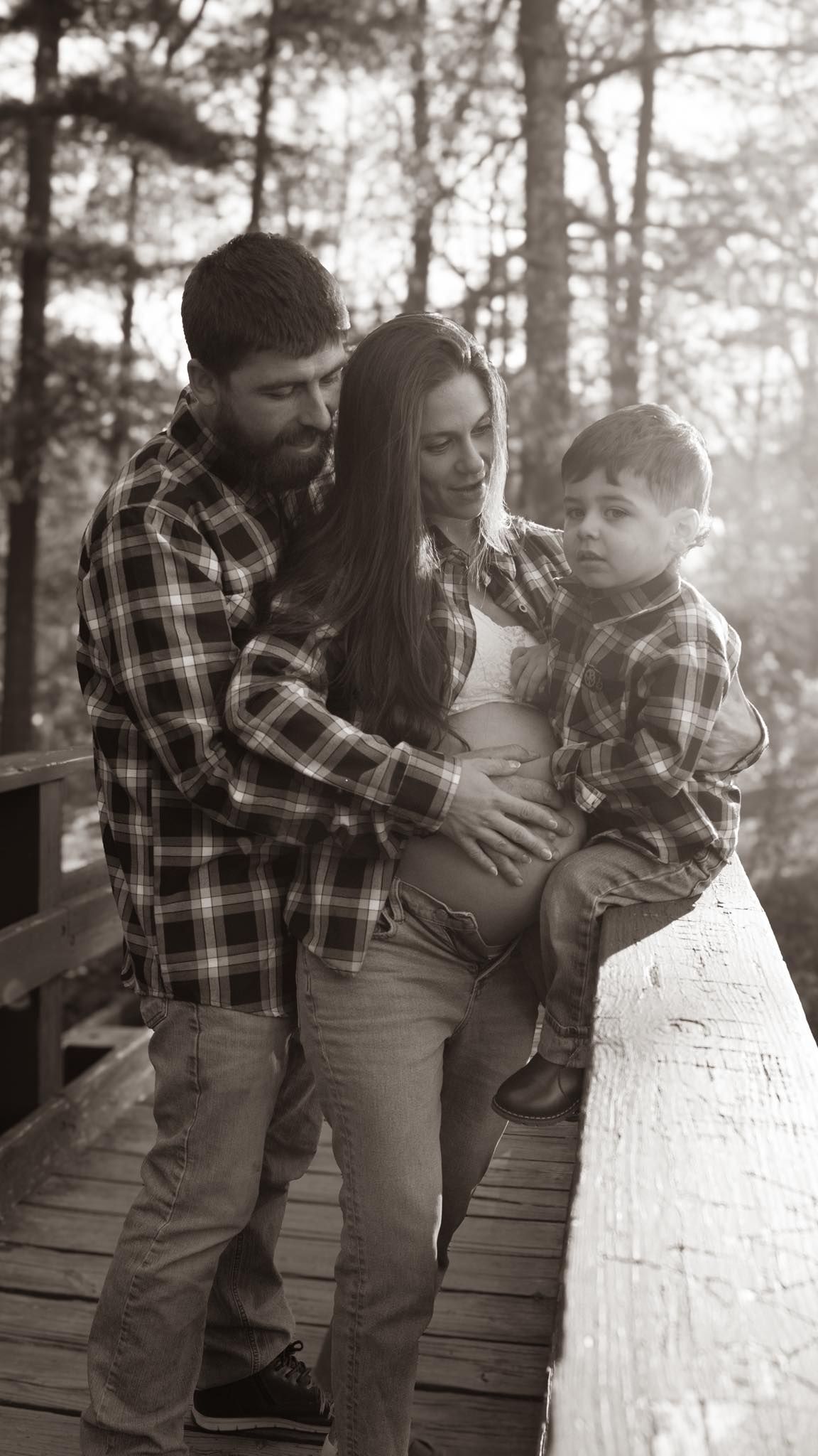 Black and white family portrait on wooden steps in forest setting.