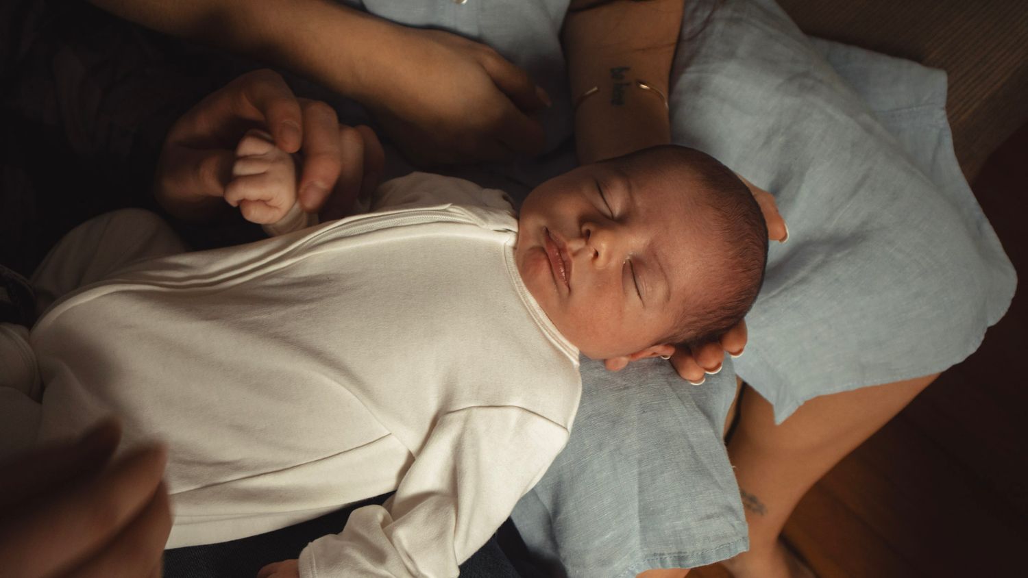 Tender moment between parent and sleeping newborn on white bedding.