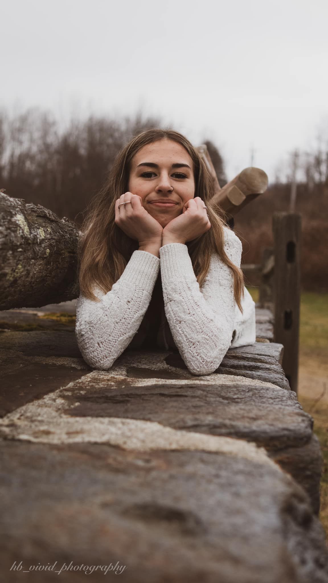 Person in white sweater resting on rock with lake view.
