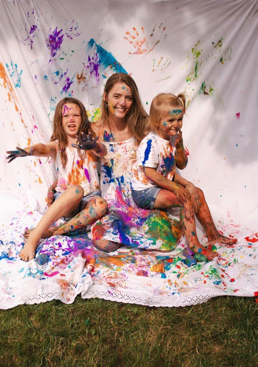 Joyful paint splatter photoshoot with colorful handprints on white backdrop.