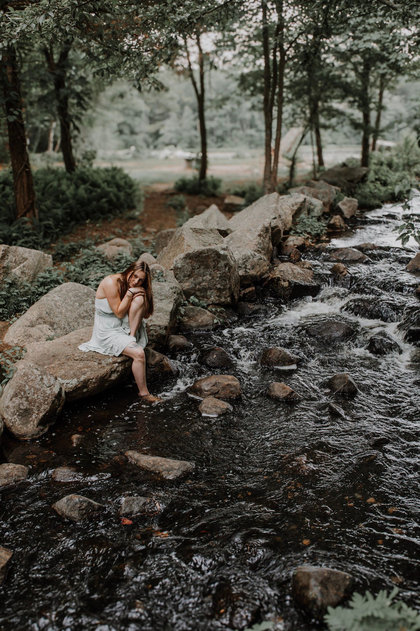 A tranquil forest creek scene with rocks and rushing water captured in moody black and white tones.