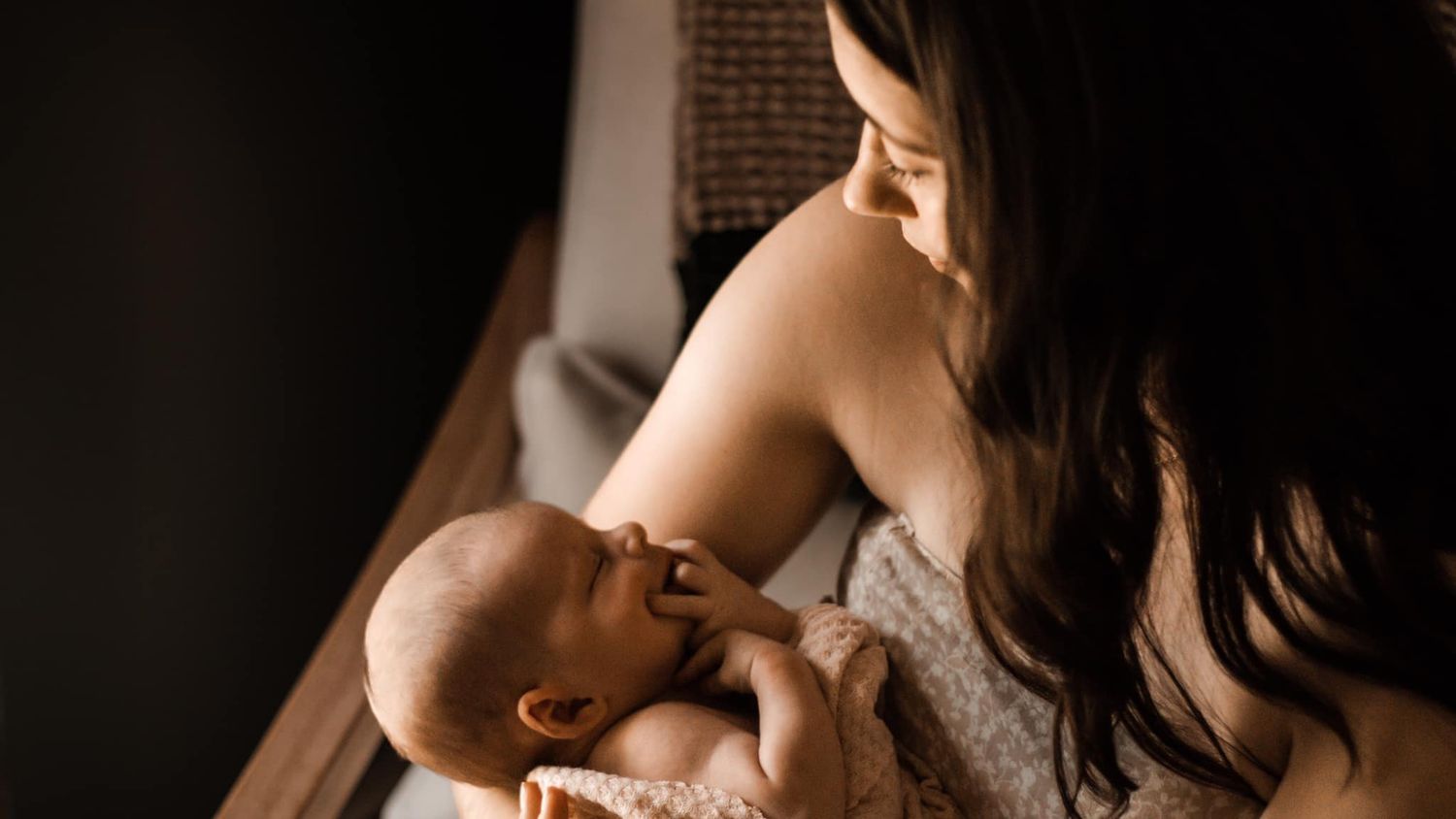 A tender moment between parent and baby in a white dress against a dark background.