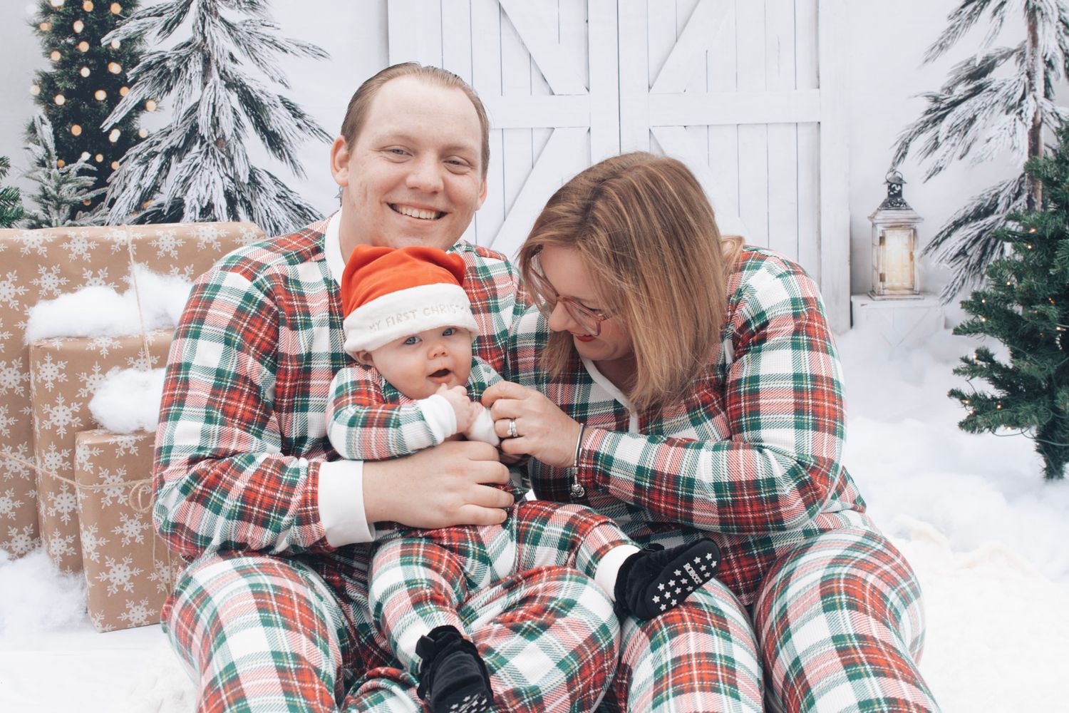 Family in coordinating plaid holiday pajamas enjoying playful moments in snowy setting.