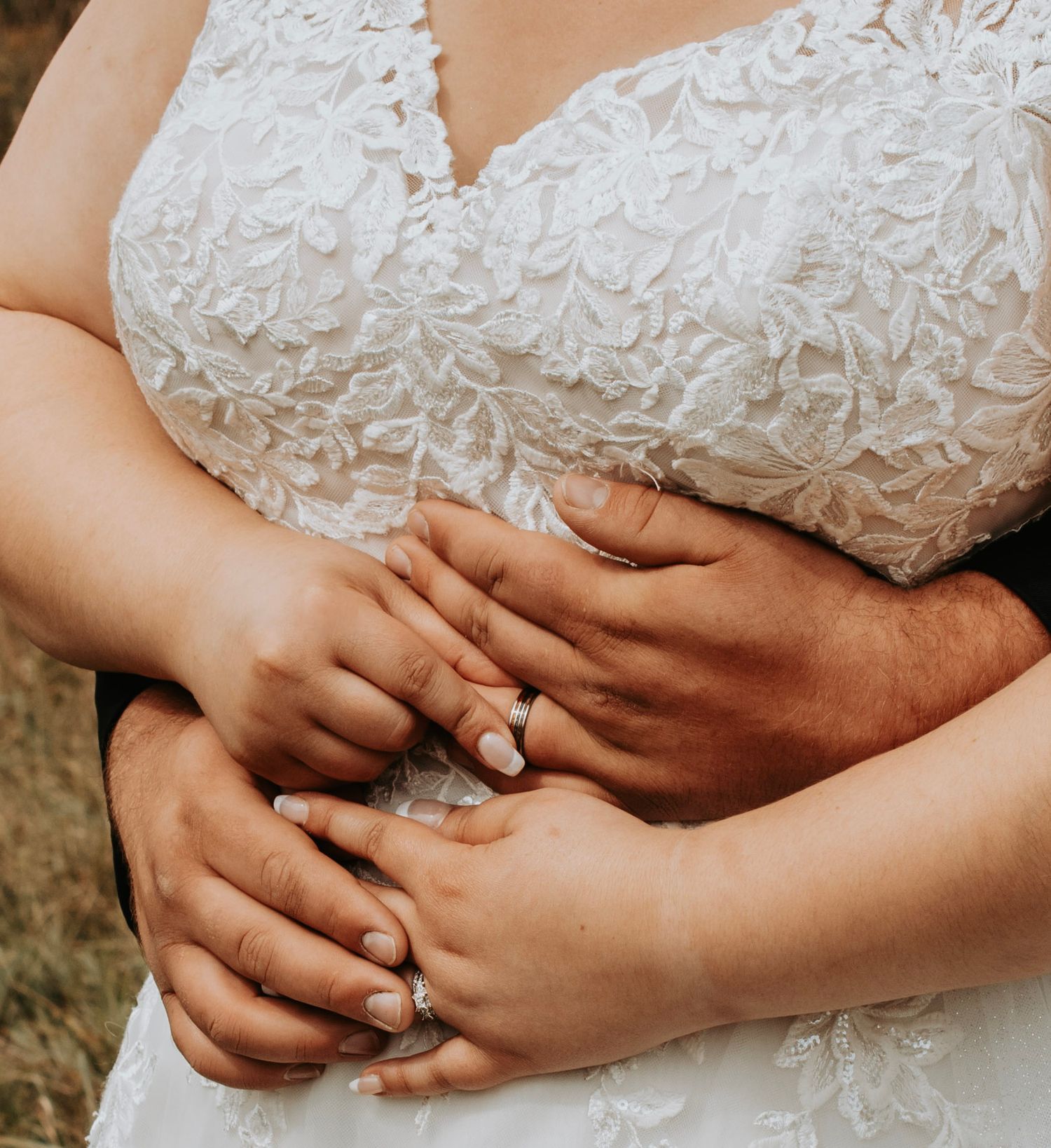 Close up of hands with wedding rings against a white lace dress.
