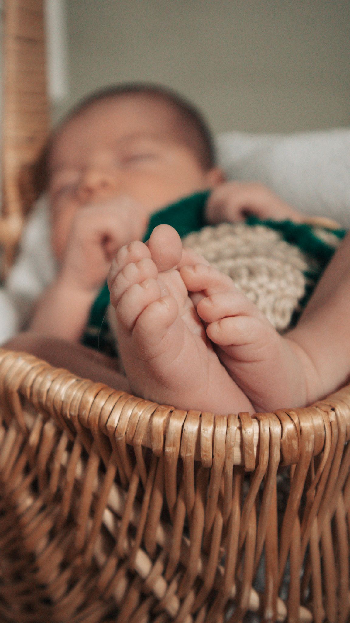 Tiny baby feet resting in a woven wicker basket with soft lighting and shallow depth of field.