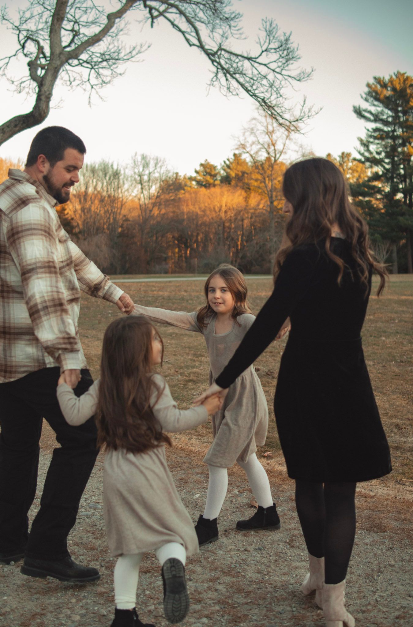A family dances together in a field at sunset during autumn while wearing casual clothing.