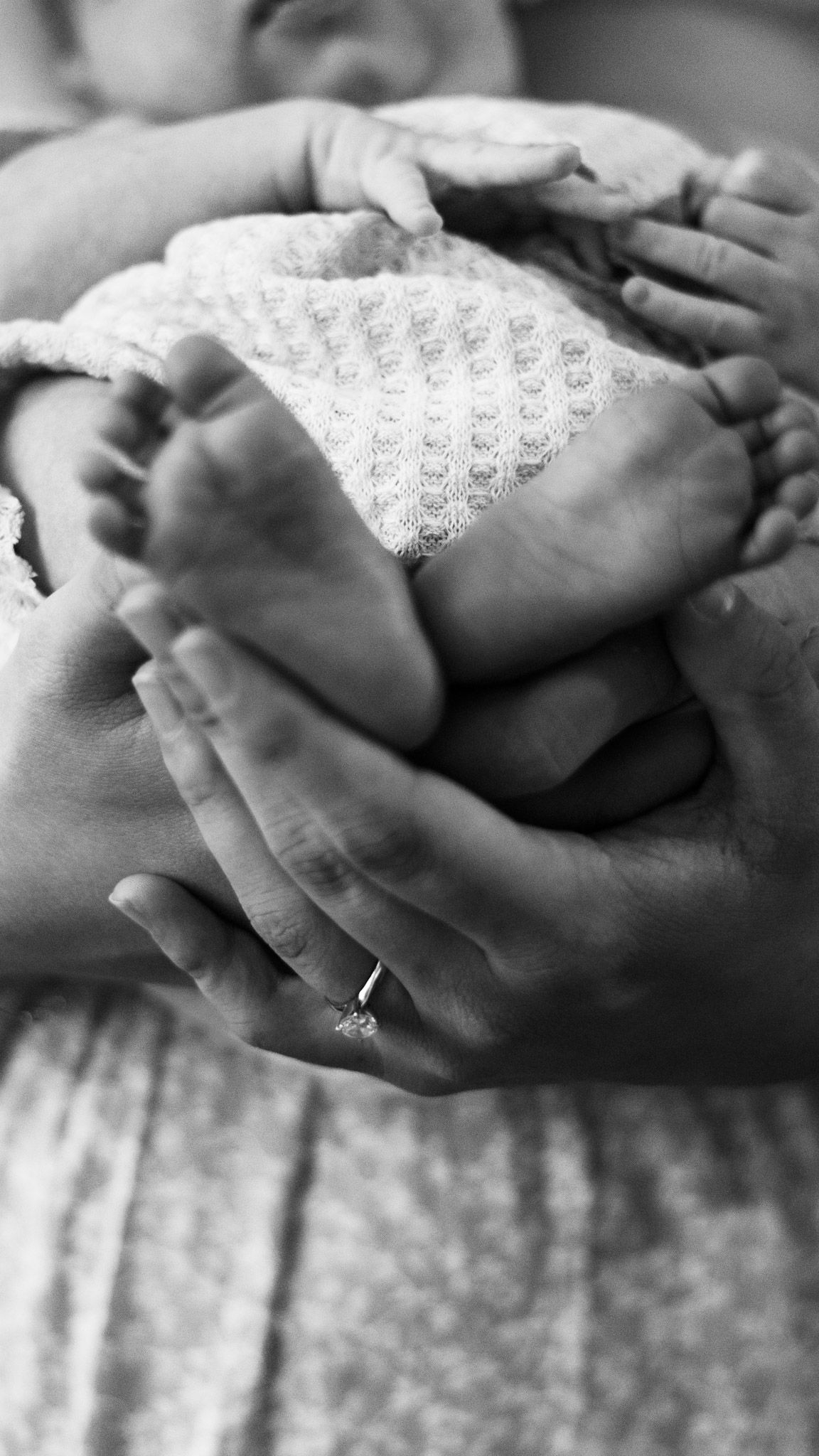 Black and white close-up of tiny baby feet being gently held in adult hands.